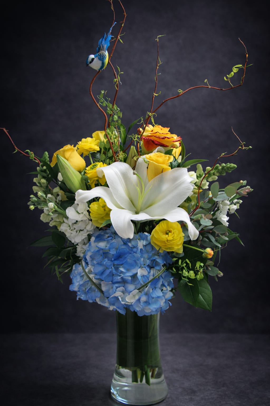 Bouquet of white lilies, yellow roses, and blue hydrangea in a glass vase