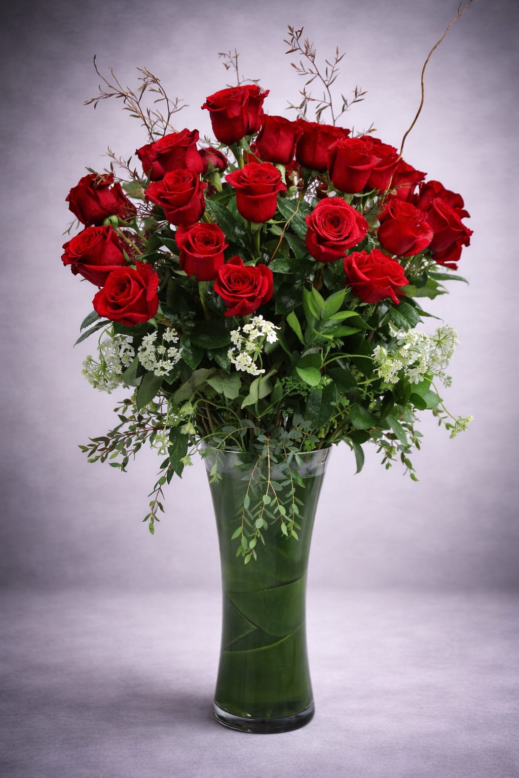 Red roses arranged in a tall glass vase with white filler flowers
