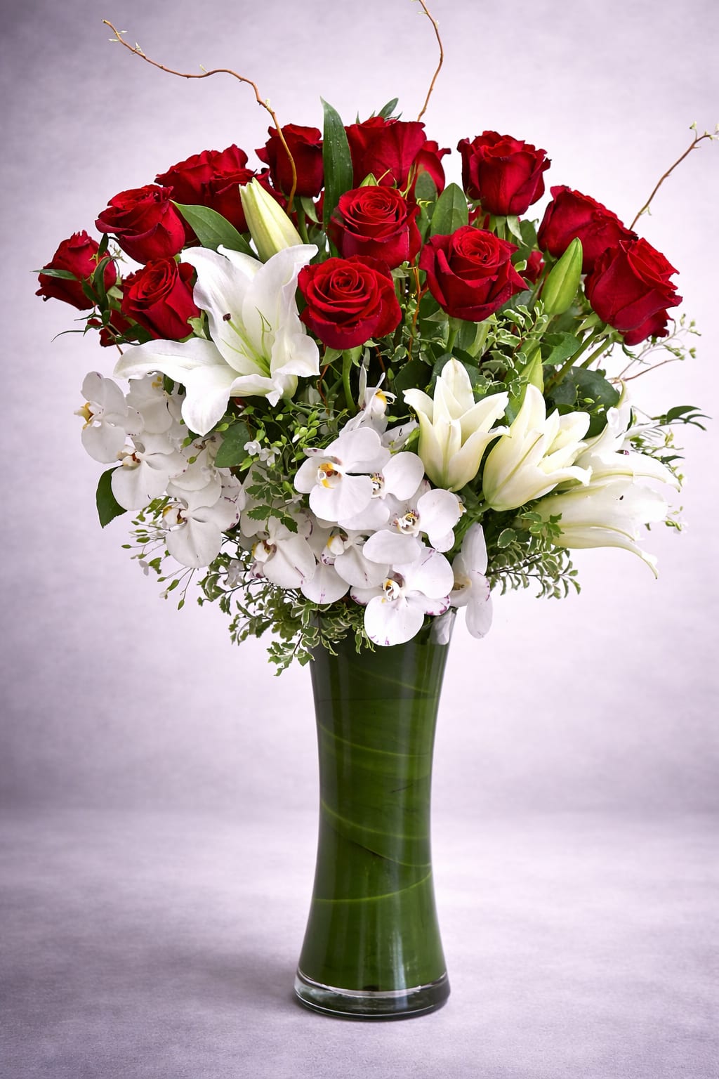 Red roses and white lilies with orchids in a tall green vase