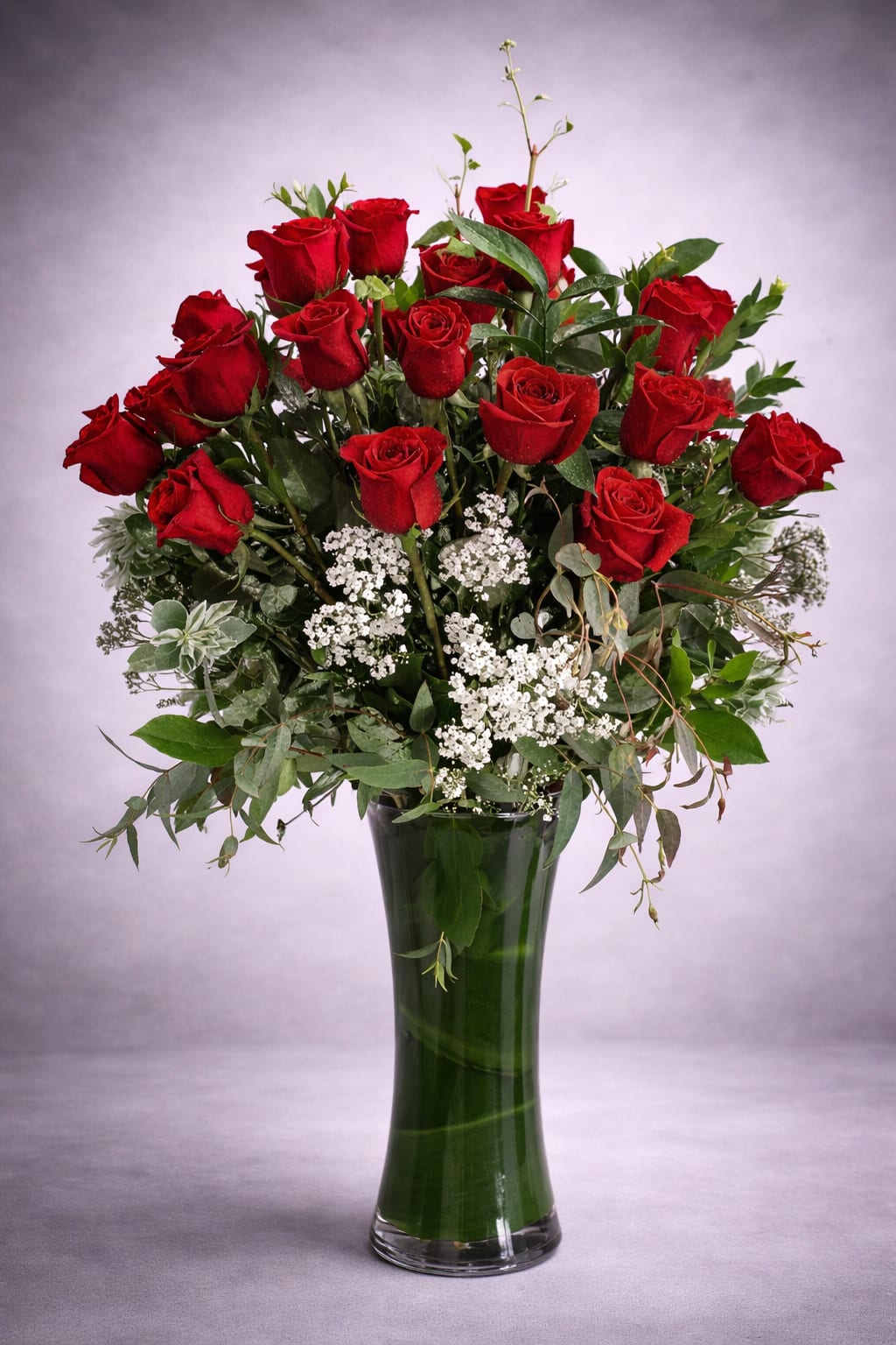 Red roses arranged in a tall glass vase with white filler flowers