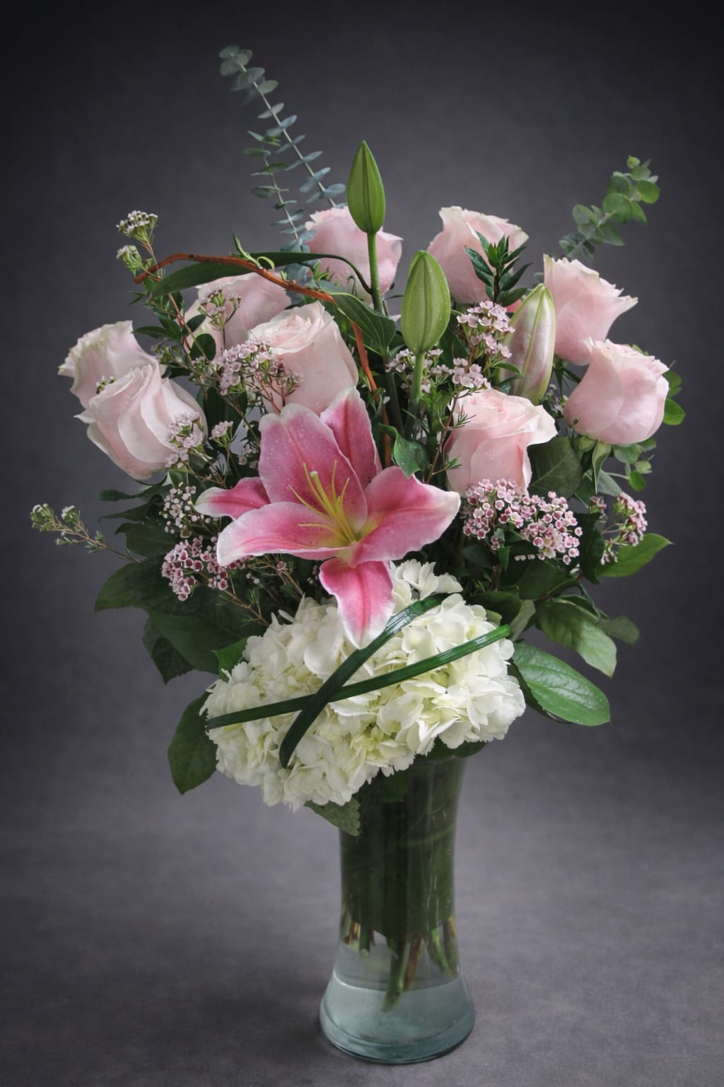 Pink lilies and roses arranged with white hydrangea in a glass vase