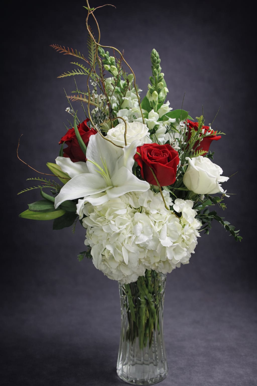Red and white roses with lilies and hydrangeas in a glass vase