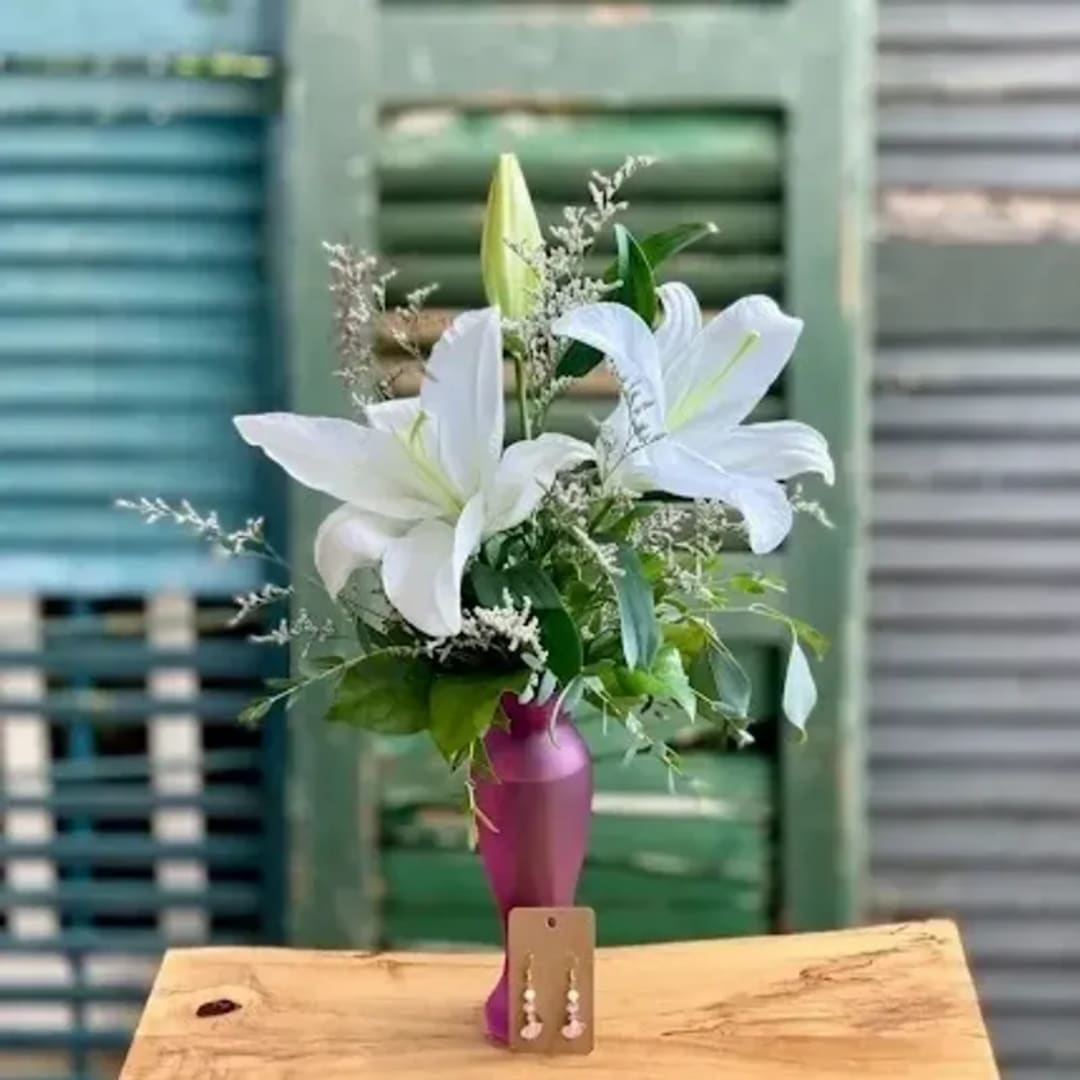 White lilies in a purple vase with a pair of earrings on a card