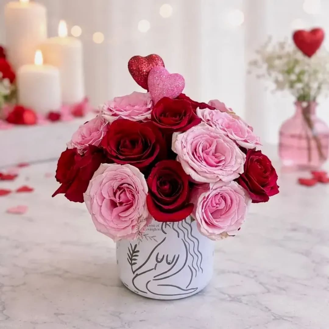 Pink and red roses arranged in a white vase with heart picks