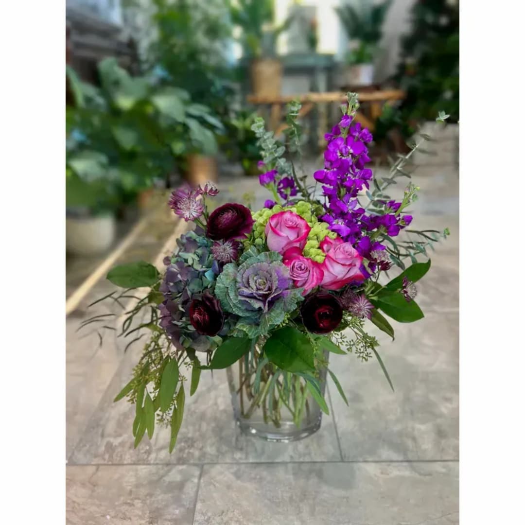 Mixed bouquet of pink roses, purple blooms, and greenery in a glass vase