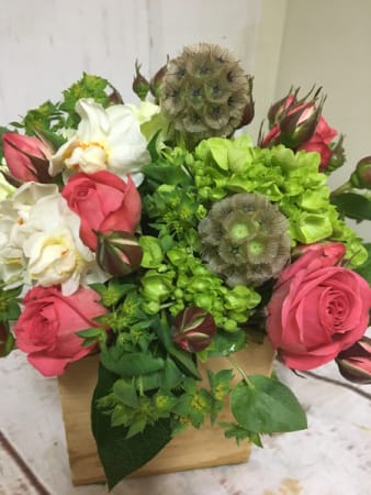 Compact arrangement of pink roses, white blooms, and green hydrangeas in a small wooden box