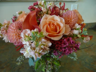Peach roses and dahlias with pink accent flowers arranged in a clear glass vase