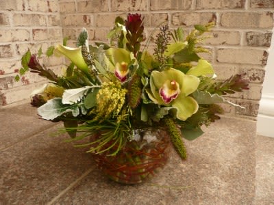 Low arrangement of green cymbidium orchids and pale calla lilies in a clear glass bowl vase