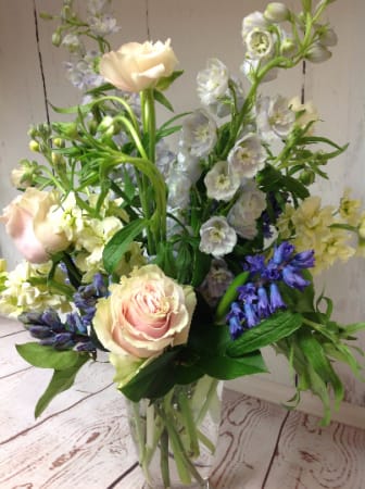 Tall mixed bouquet of pale pink roses and soft blue flowers in a clear glass vase