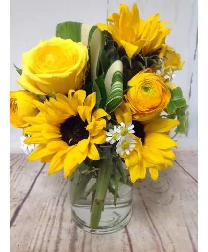 Yellow sunflowers, rose, and ranunculus arranged in a clear glass jar vase
