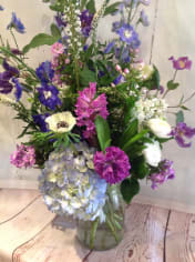 Tall mixed bouquet of purple, blue, pink, and white flowers in a clear glass vase