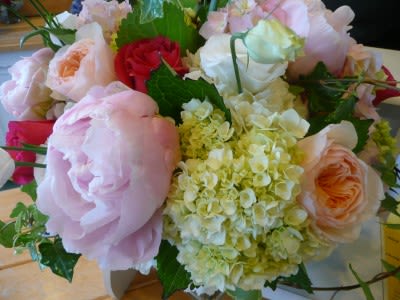 Round arrangement of pale pink peonies, roses, and cream hydrangeas with accents of red roses