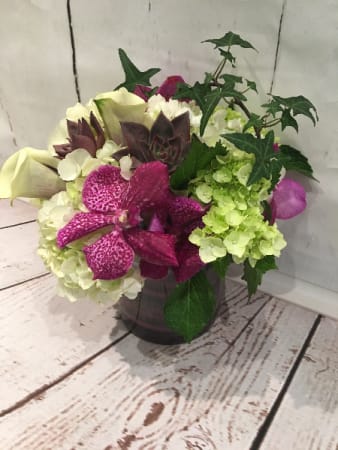 Low arrangement of white and green hydrangeas with bright pink orchids and calla lilies in a glass vase with trailing ivy
