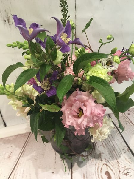 Loose garden-style arrangement of purple and pink flowers in a round glass vase
