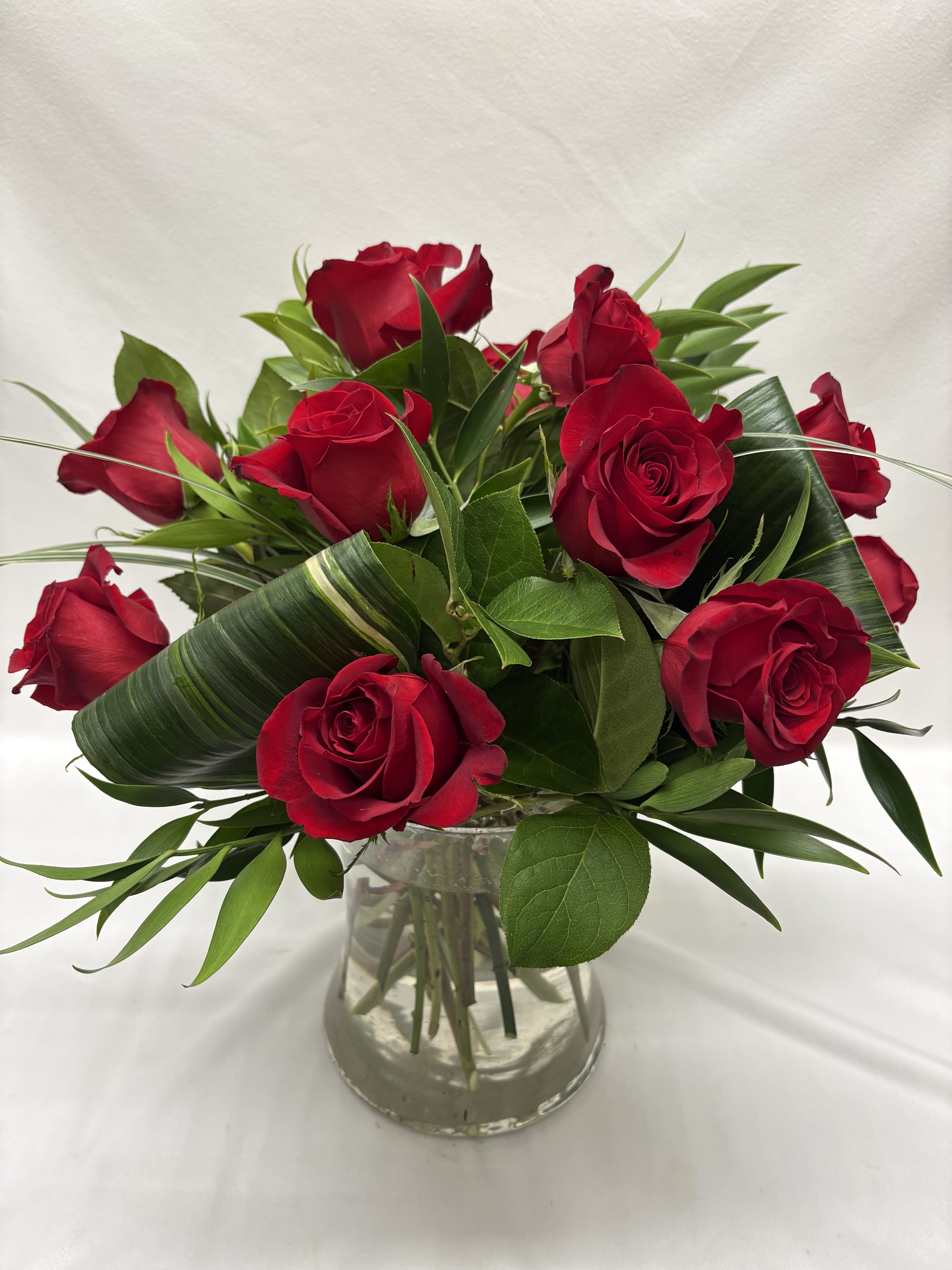 Arrangement of red roses with looped green leaves in a clear glass vase