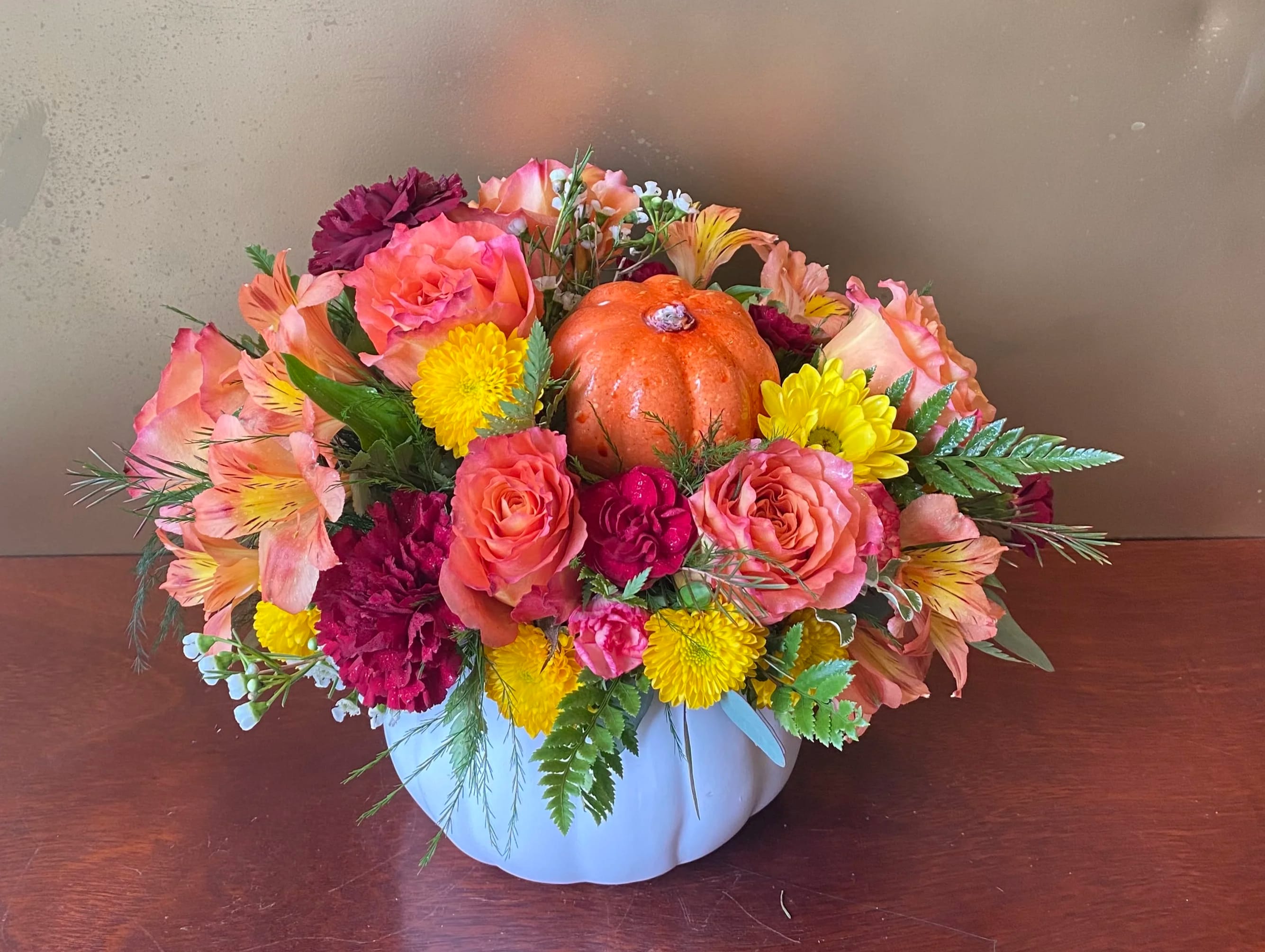 Mixed flower arrangement in a white pumpkin-shaped container with a small orange pumpkin centerpiece