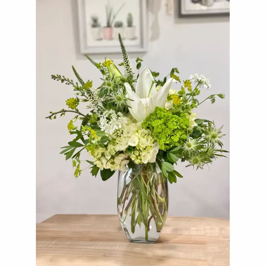 White lilies and green flowers arranged in a clear glass vase