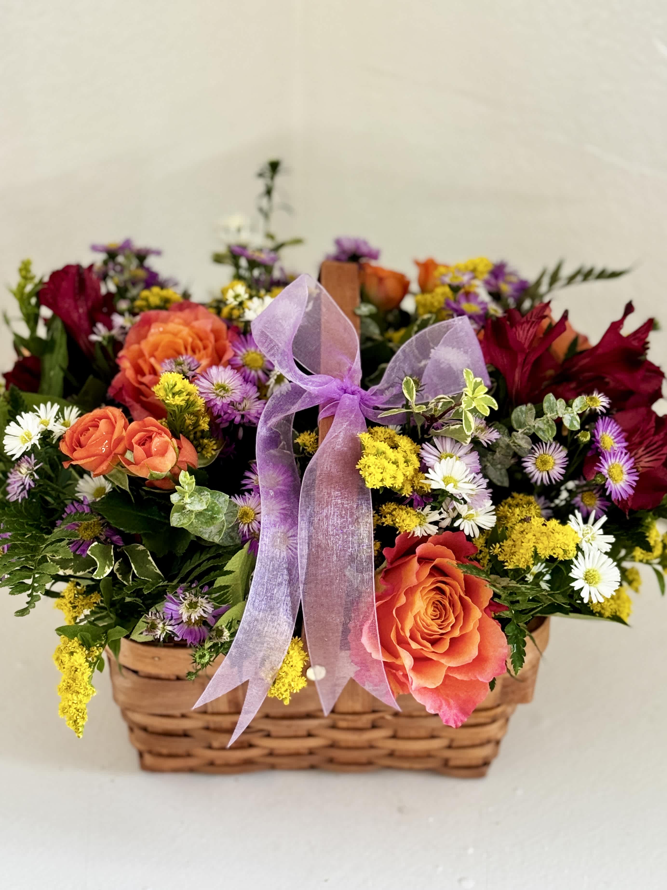 Mixed flower basket with orange roses, daisies, and a purple ribbon