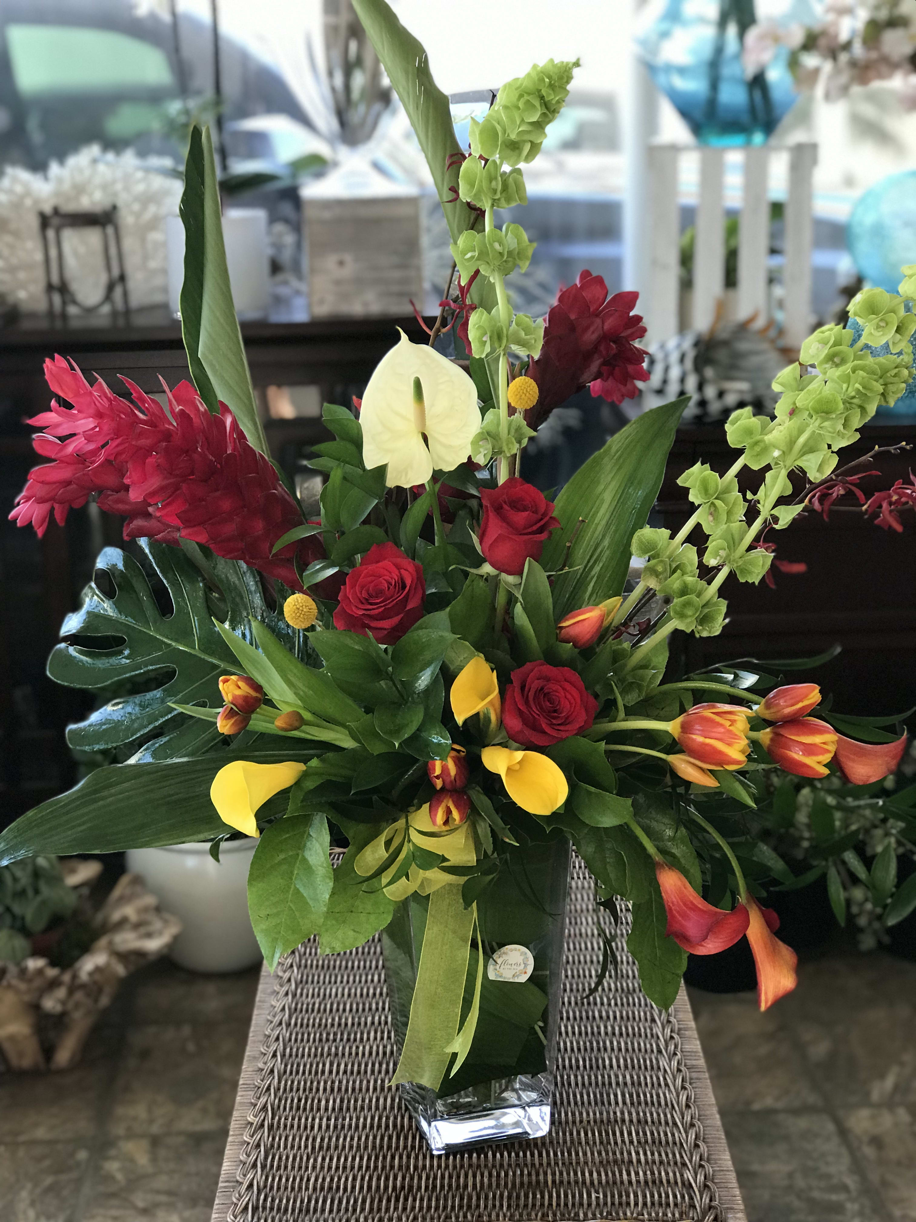 Tropical bouquet with red roses, yellow calla lilies, and green orchids in a glass vase