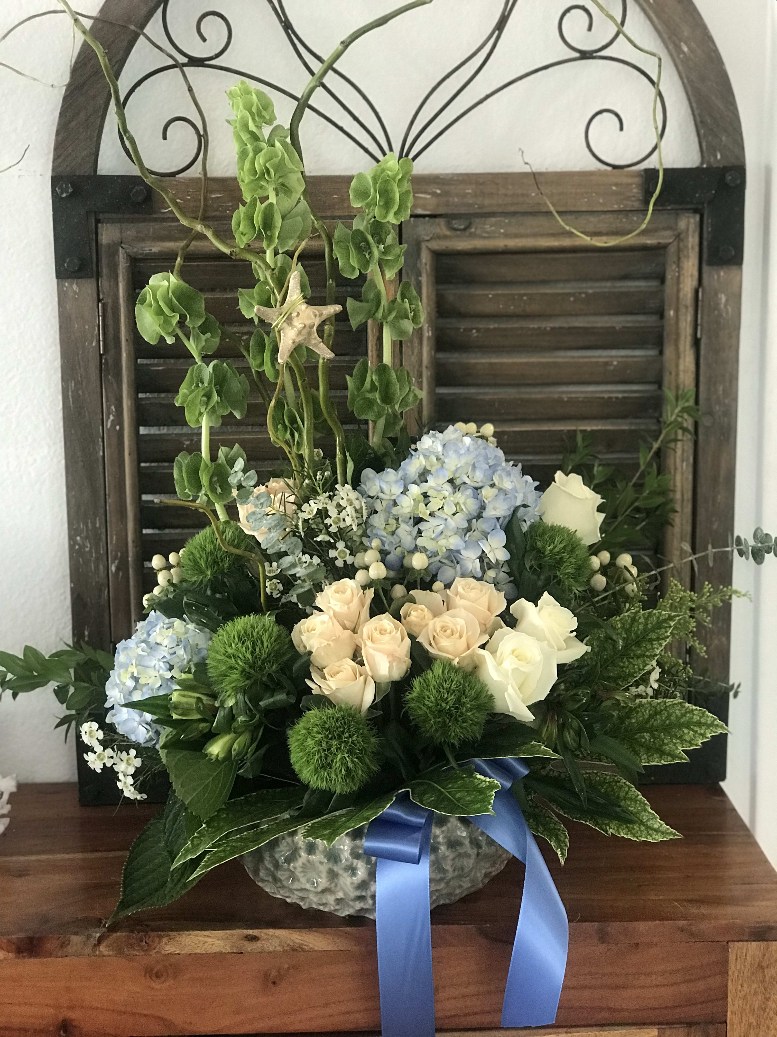 Blue hydrangeas and cream roses in a glass bowl with a blue ribbon