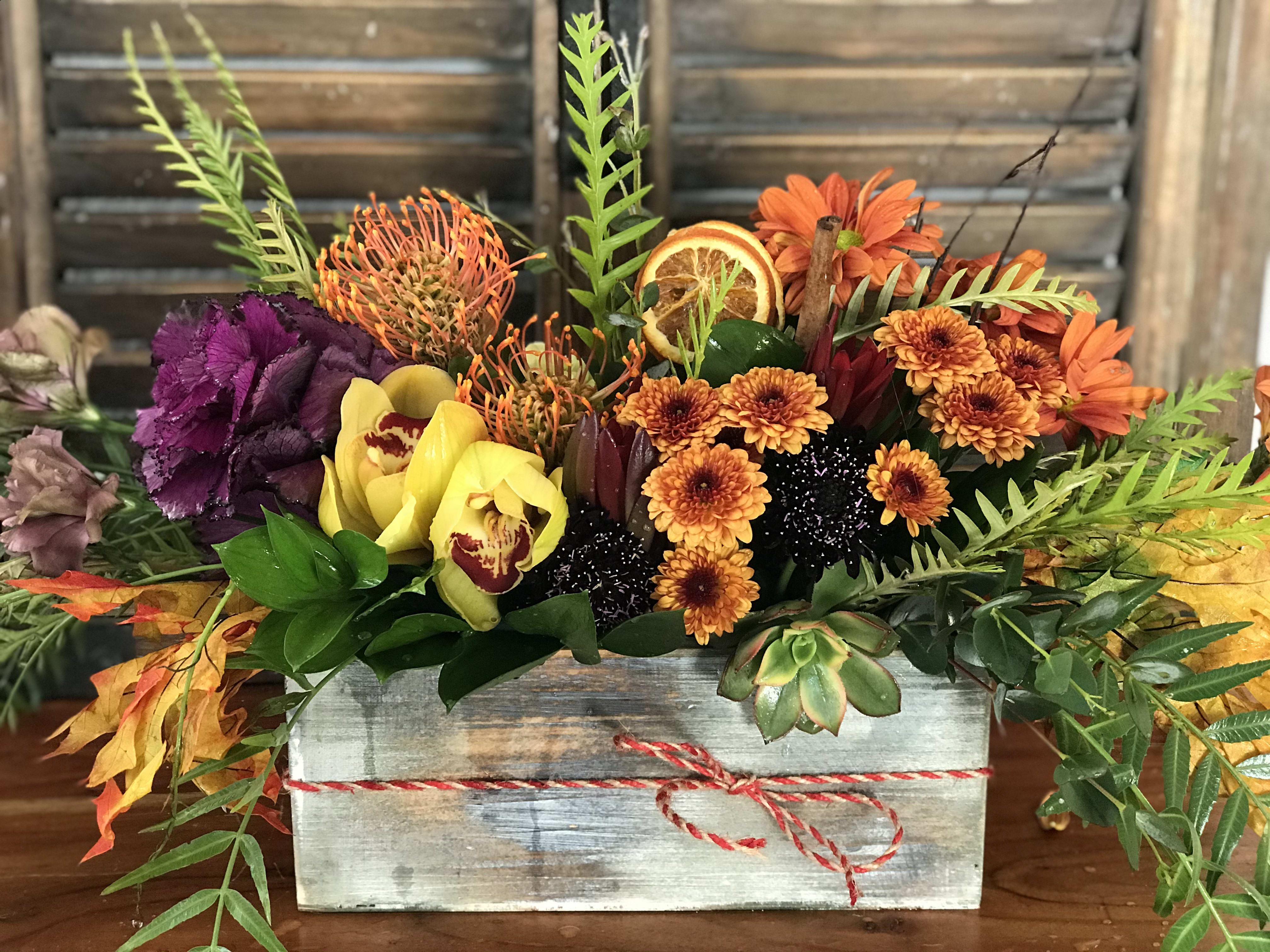 Autumn floral arrangement in a wooden box with orange, yellow, and purple blooms