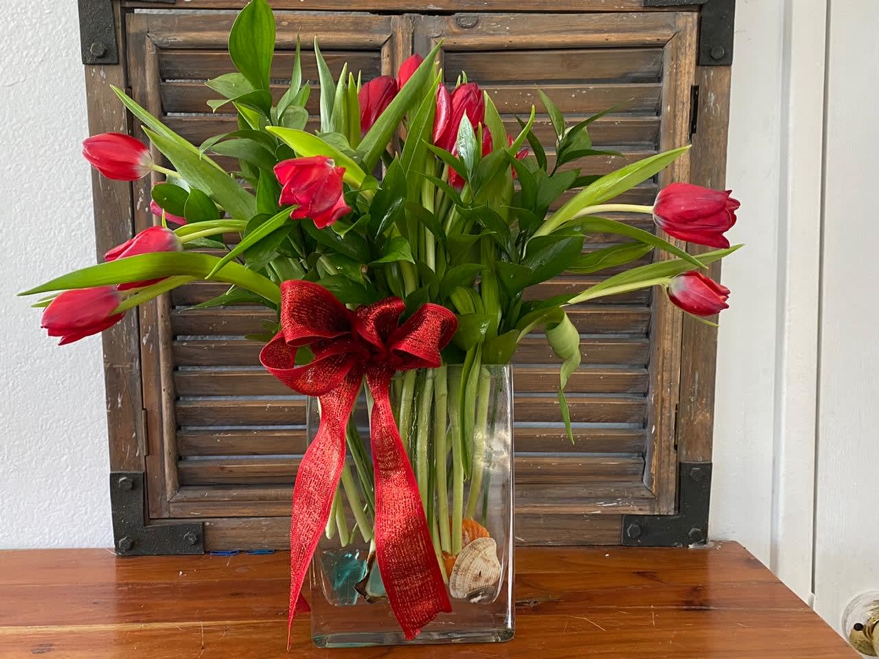 Red tulips in a clear glass vase with a red ribbon