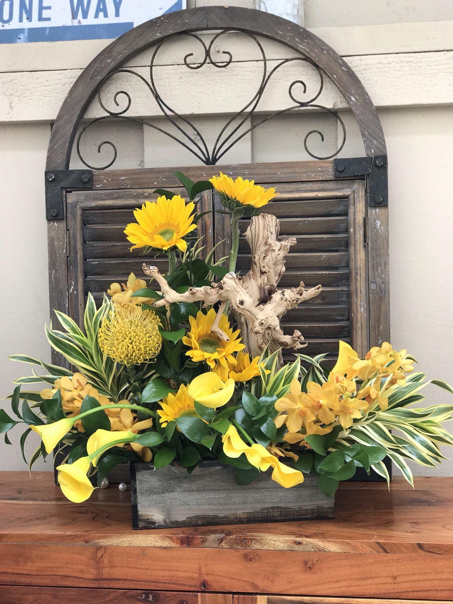 Yellow flowers arranged with calla lilies in a rustic wooden container