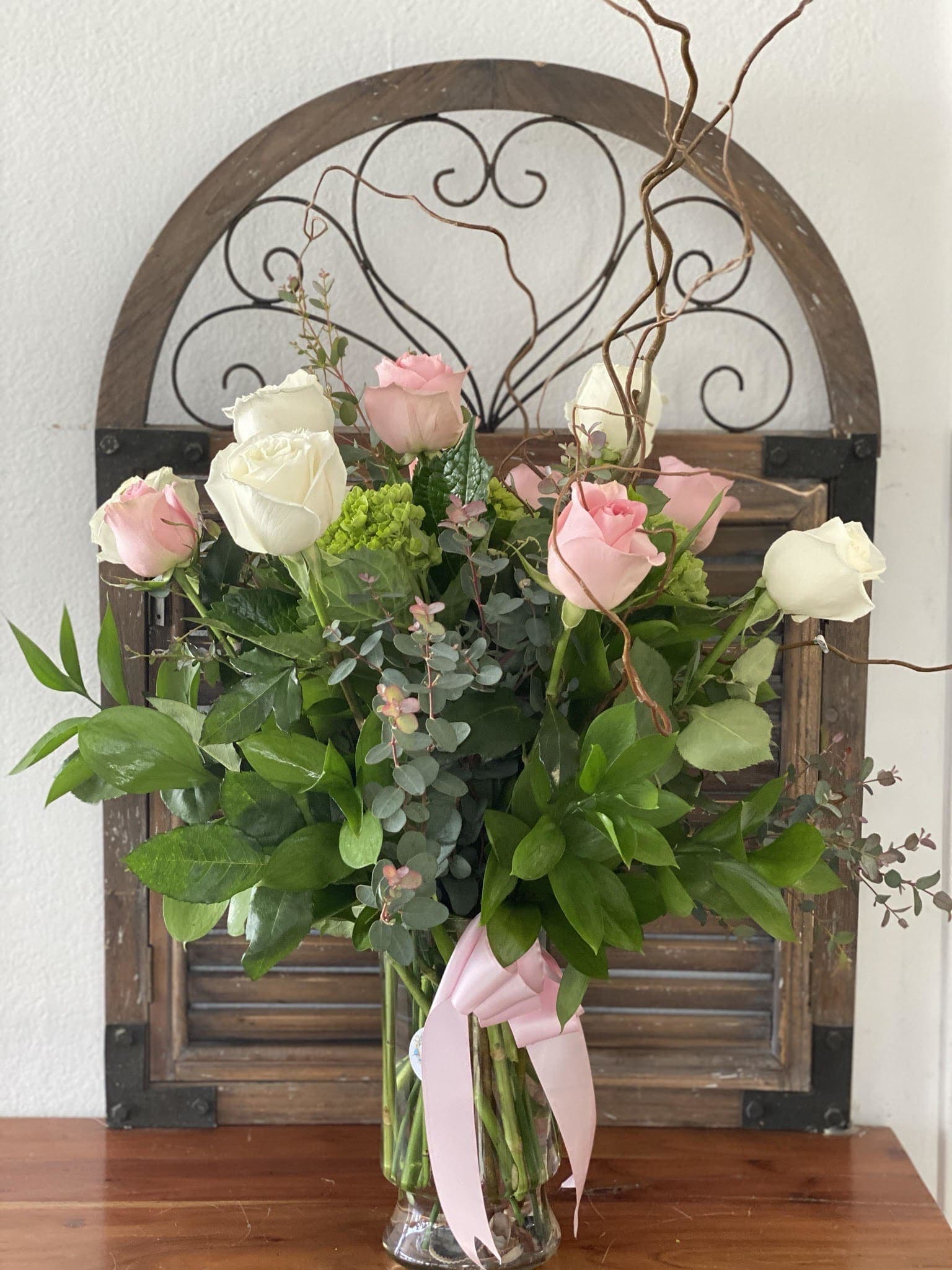 Pink and white roses in a glass vase with a pink ribbon
