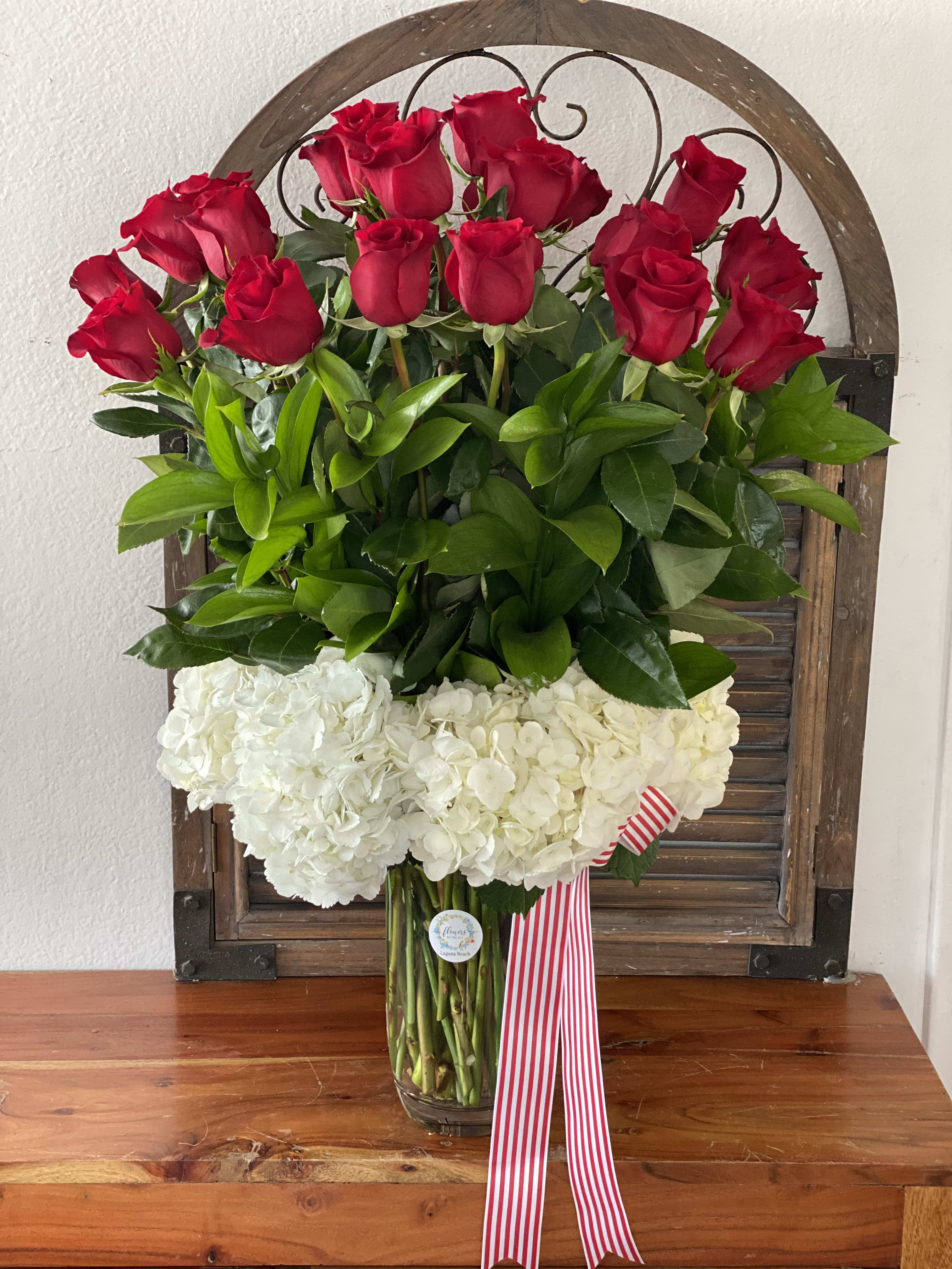 Red roses above white hydrangeas in a glass vase with a striped ribbon