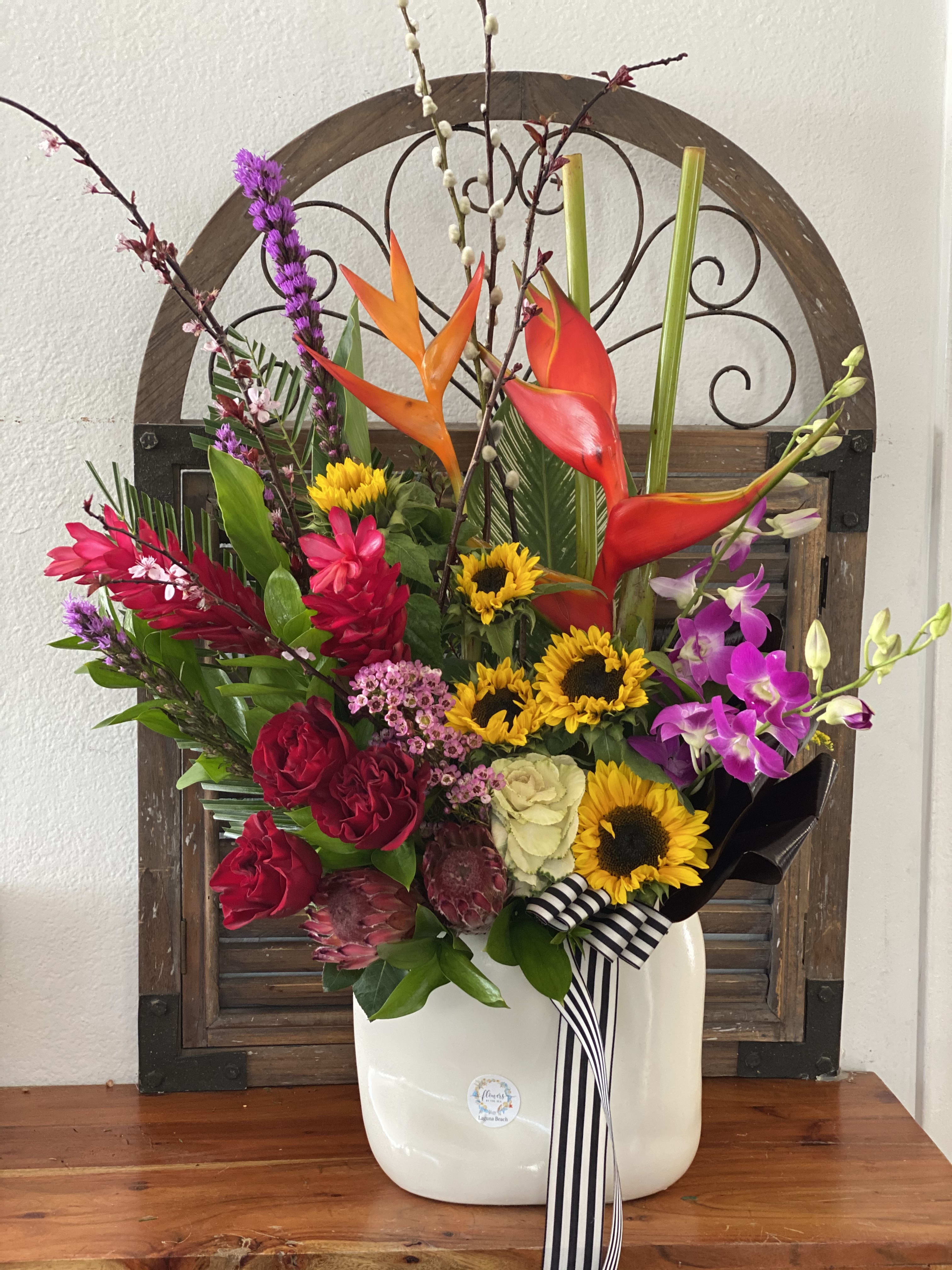 Colorful tropical flower arrangement in a white vase with a striped ribbon