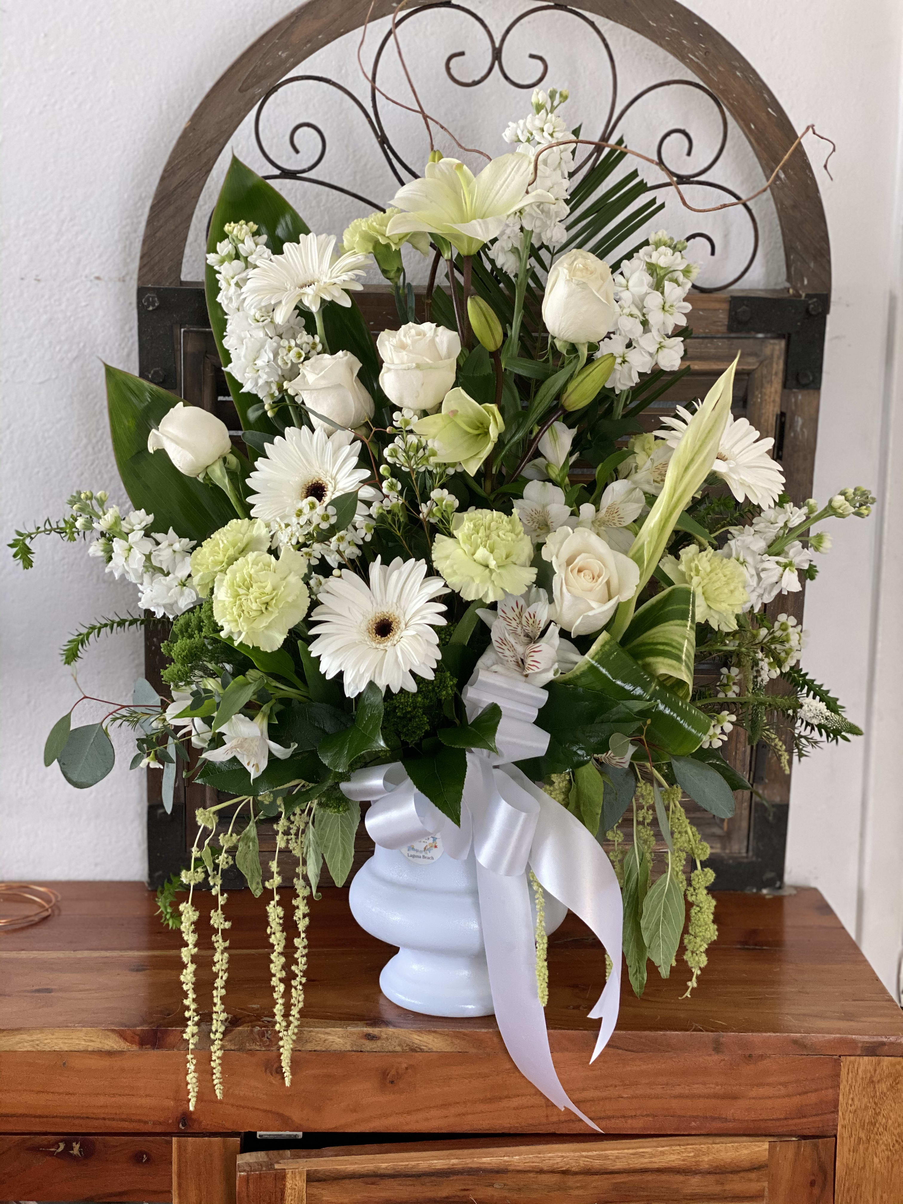 White floral arrangement in a pale blue vase with a white ribbon