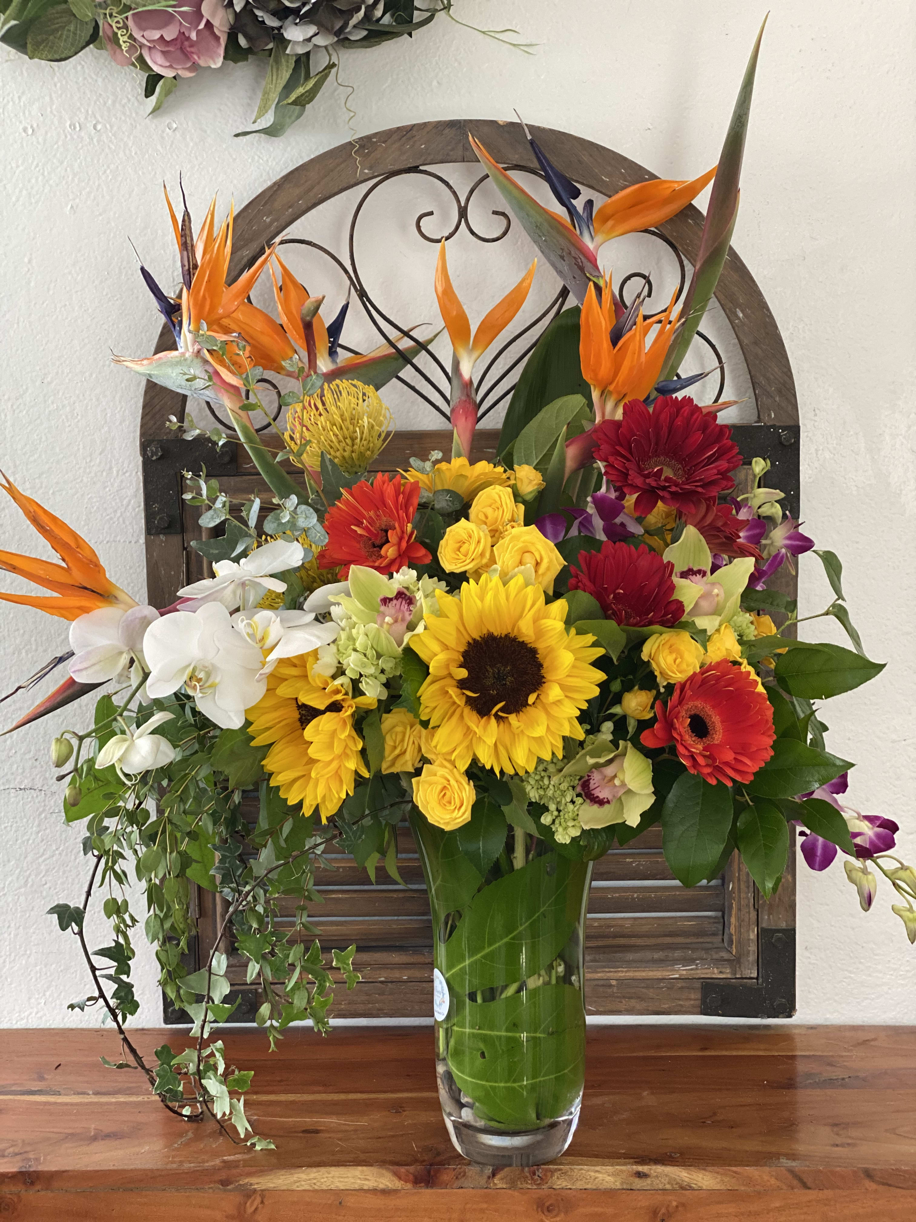 Tropical bouquet with sunflowers, orchids, and bright orange bird-of-paradise in a glass vase