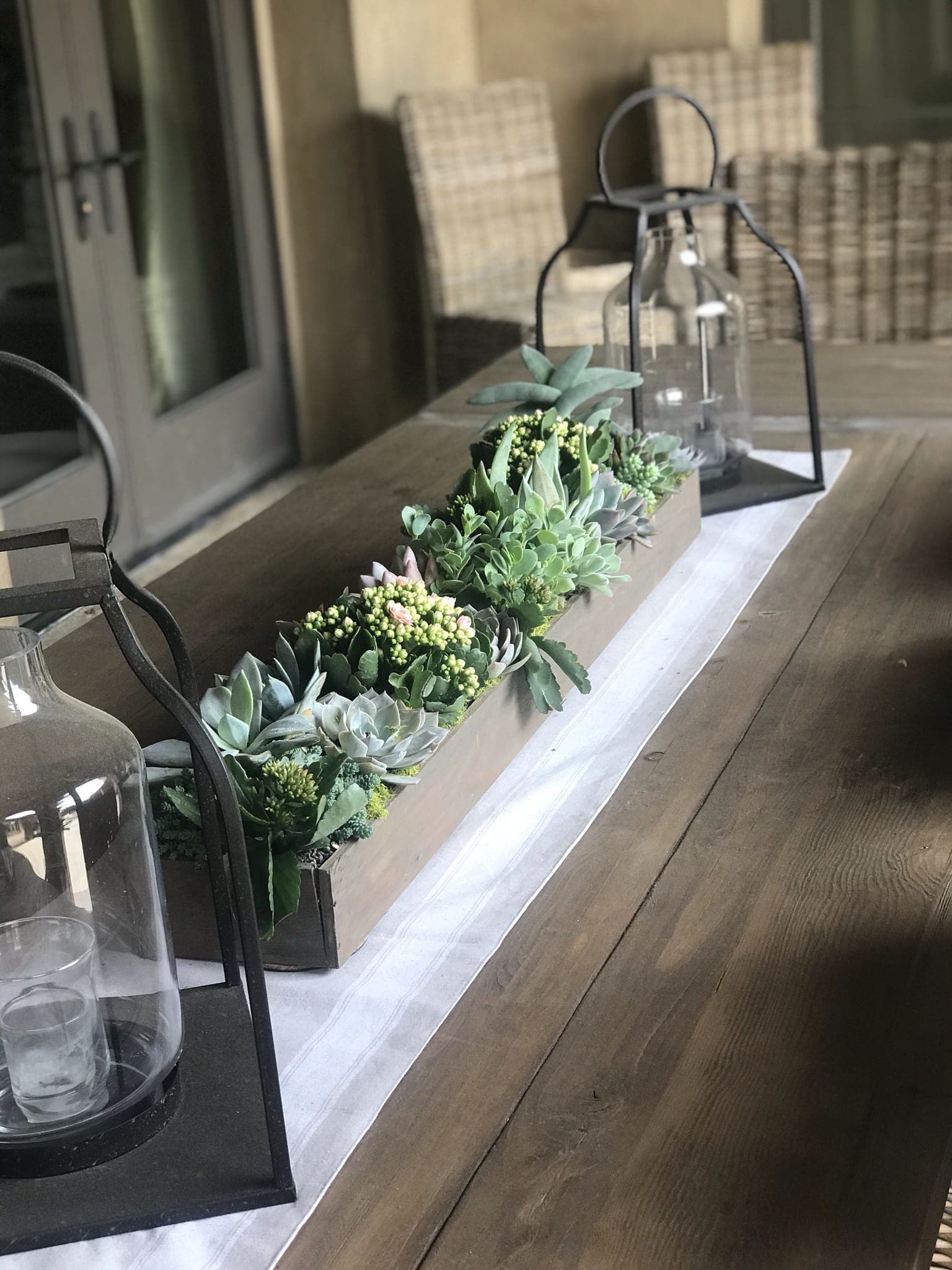 Succulent centerpiece in a long rectangular box with lanterns on a table