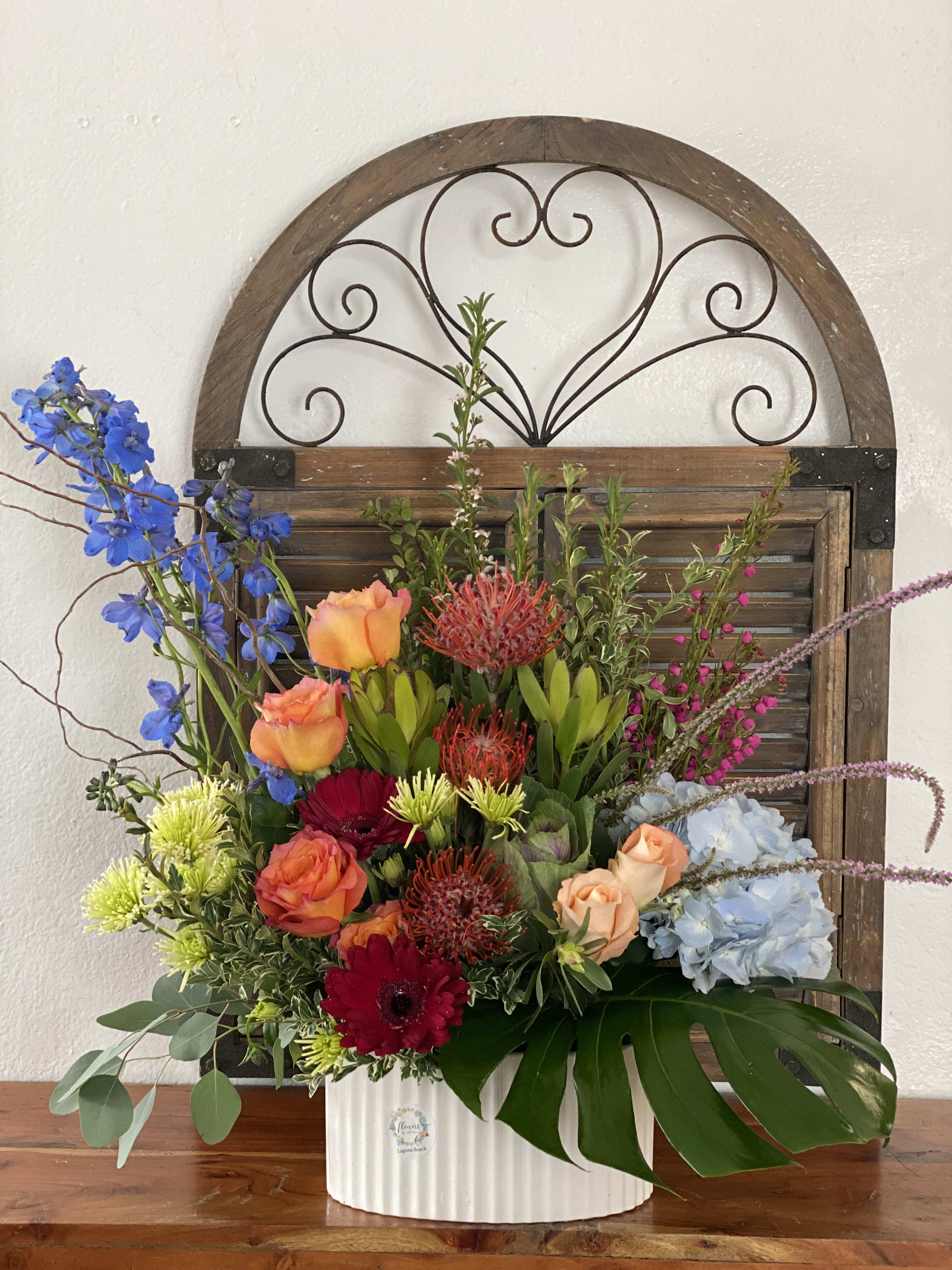 Mixed floral arrangement in a white vase with blue, orange, red, and pale blue blooms