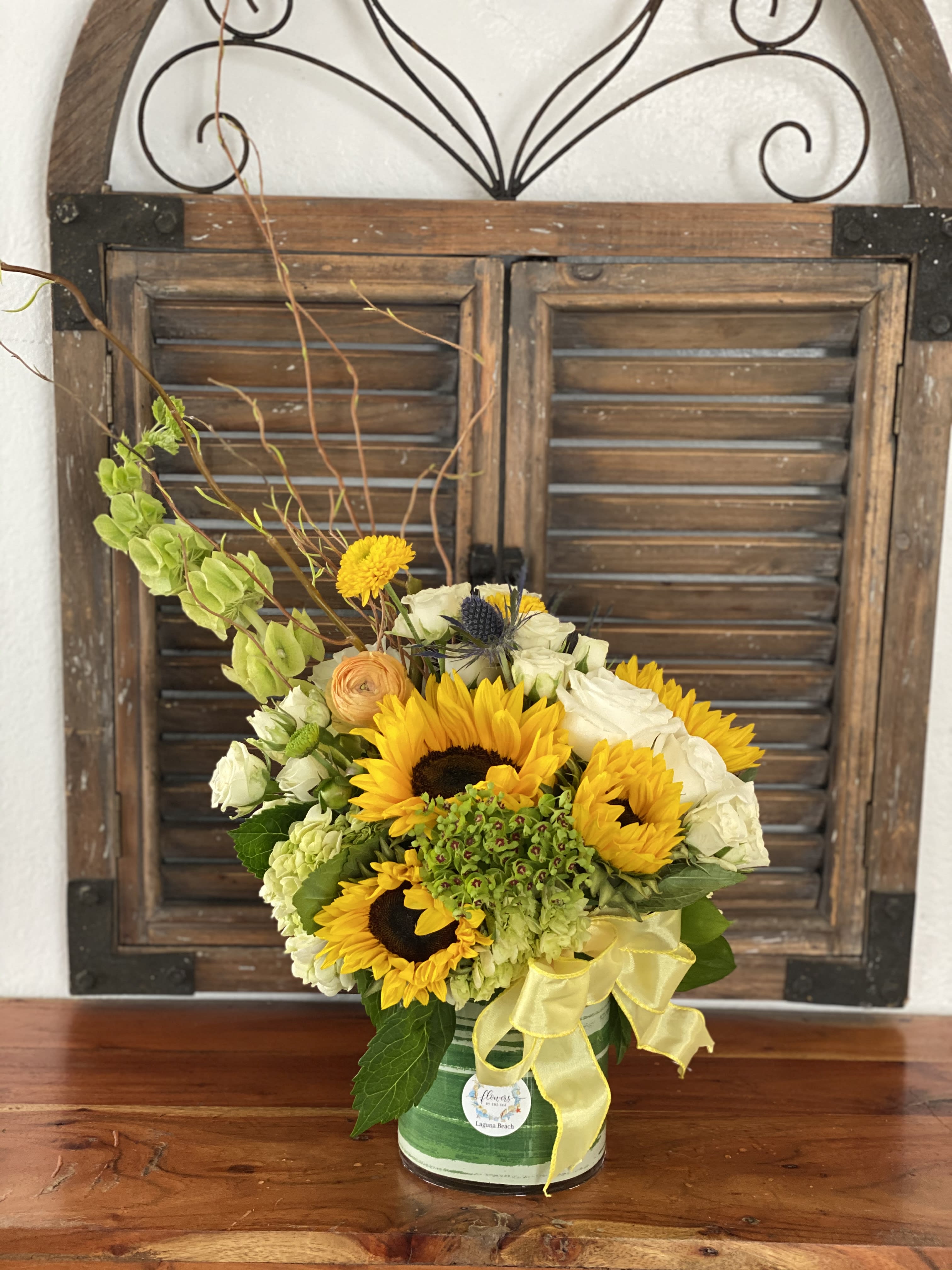 Sunflower and white rose arrangement in a striped tin container with a yellow ribbon