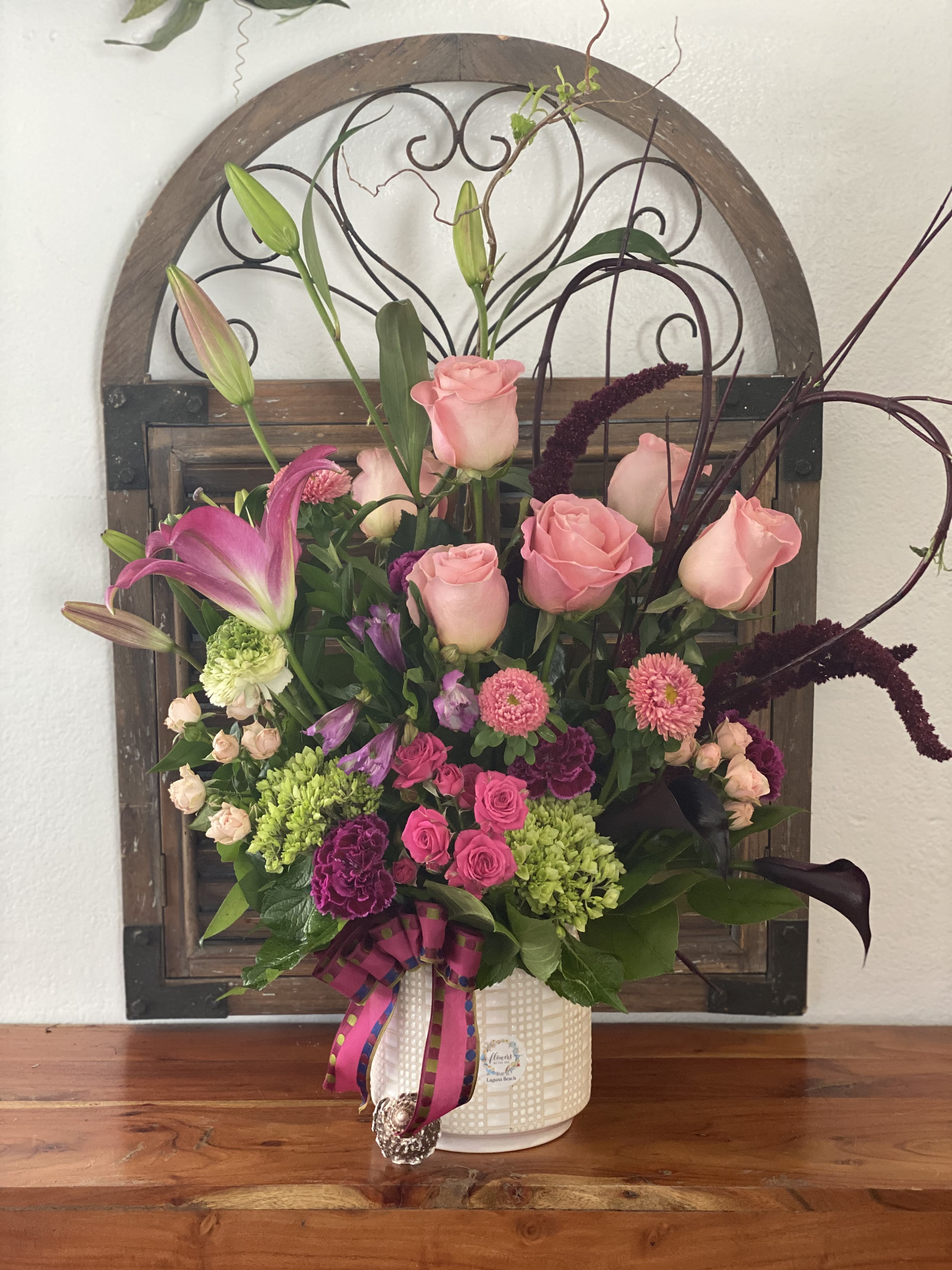 Pink roses and lilies arranged in a white vase with ribbon