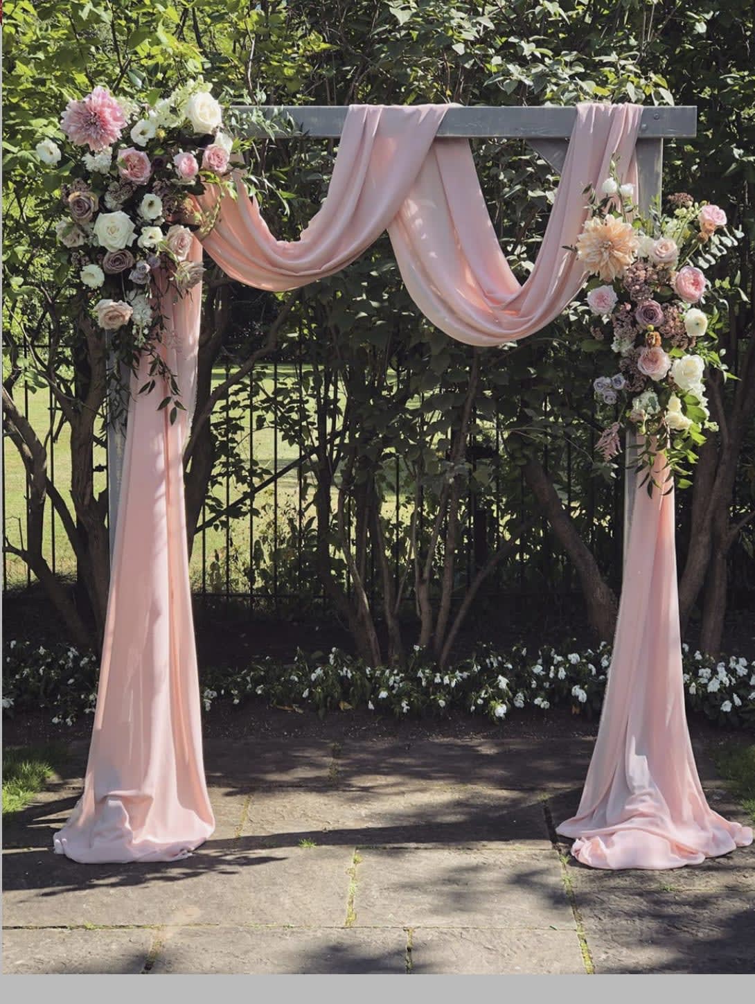 Pink draped wedding arch with pastel floral arrangements