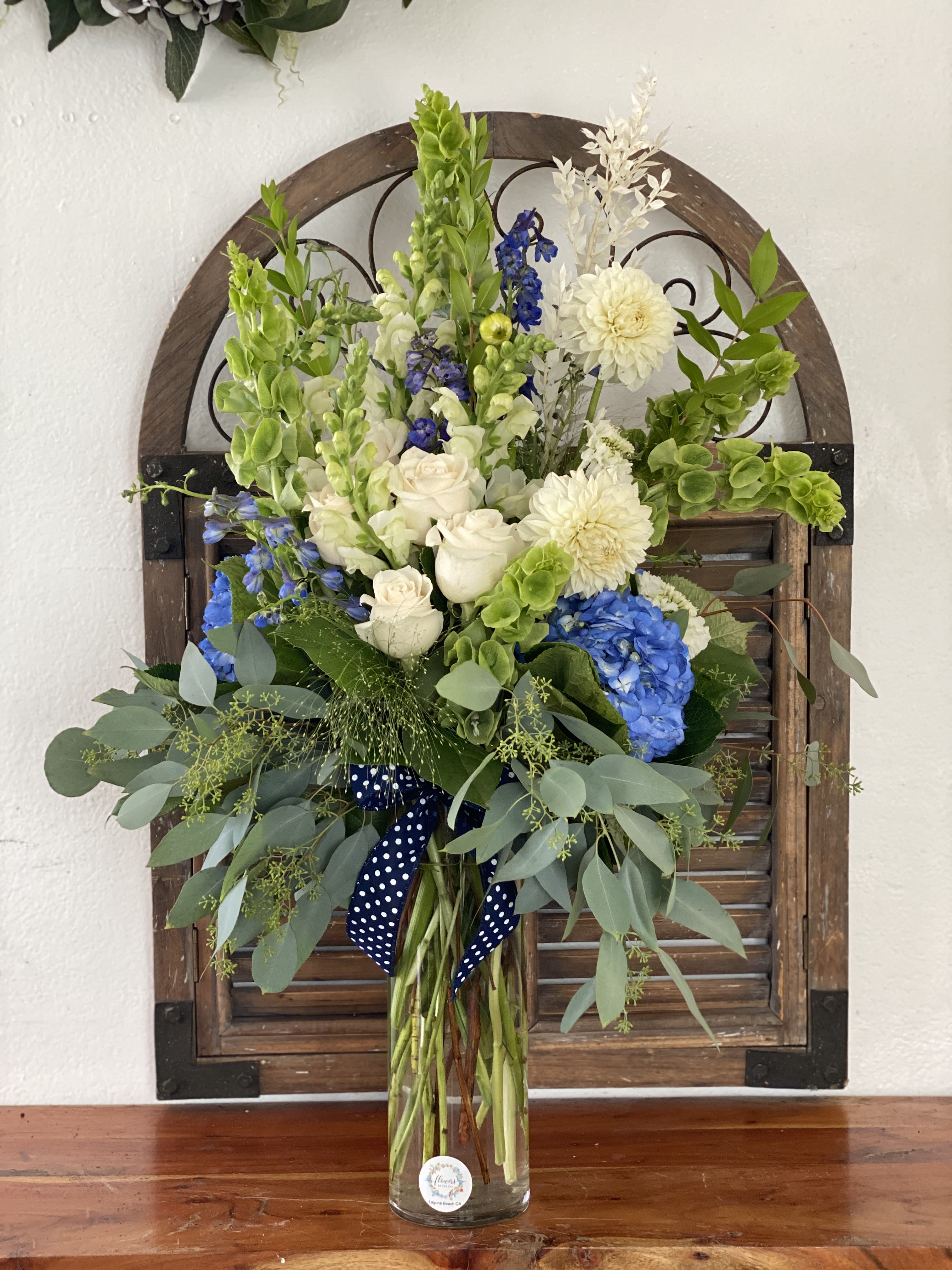Tall bouquet of white, blue, and green flowers in a glass vase