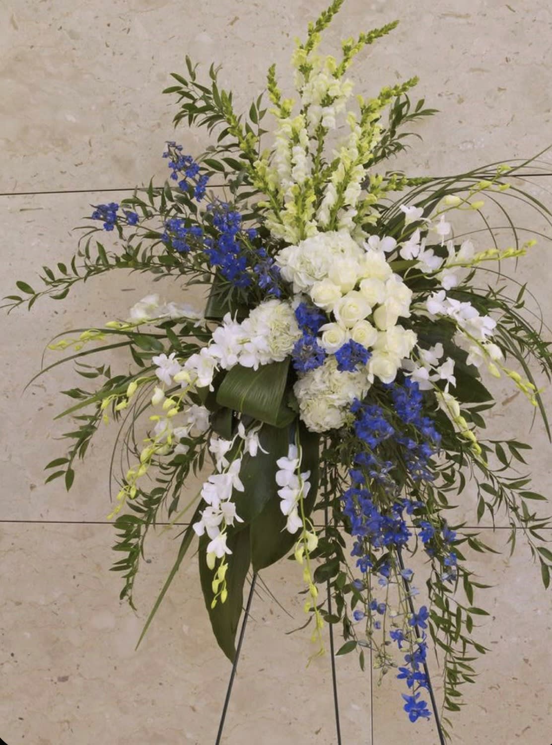 Tall white and blue floral standing spray on a black easel