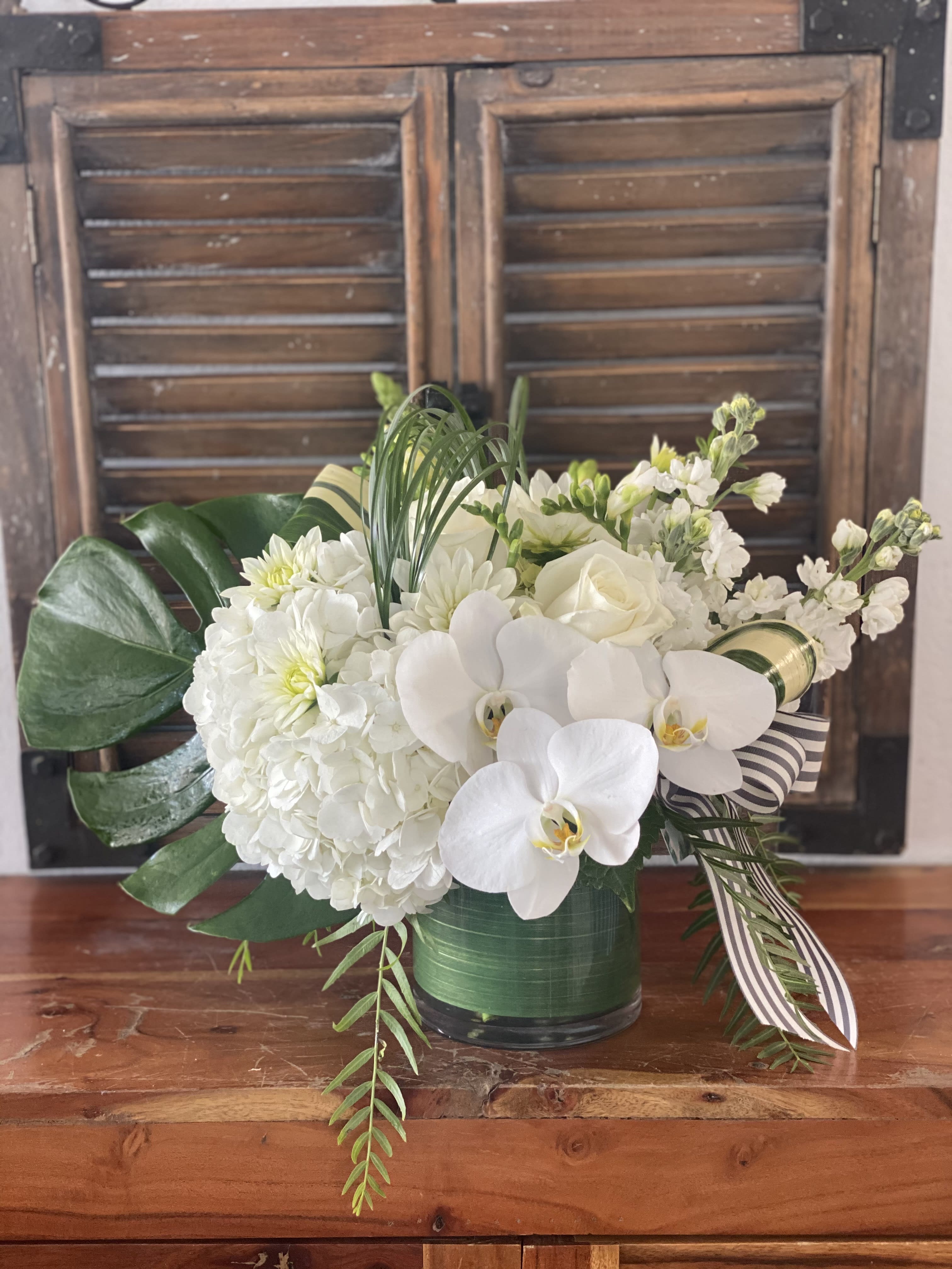 White floral arrangement with orchids, hydrangeas, and roses in a green vase