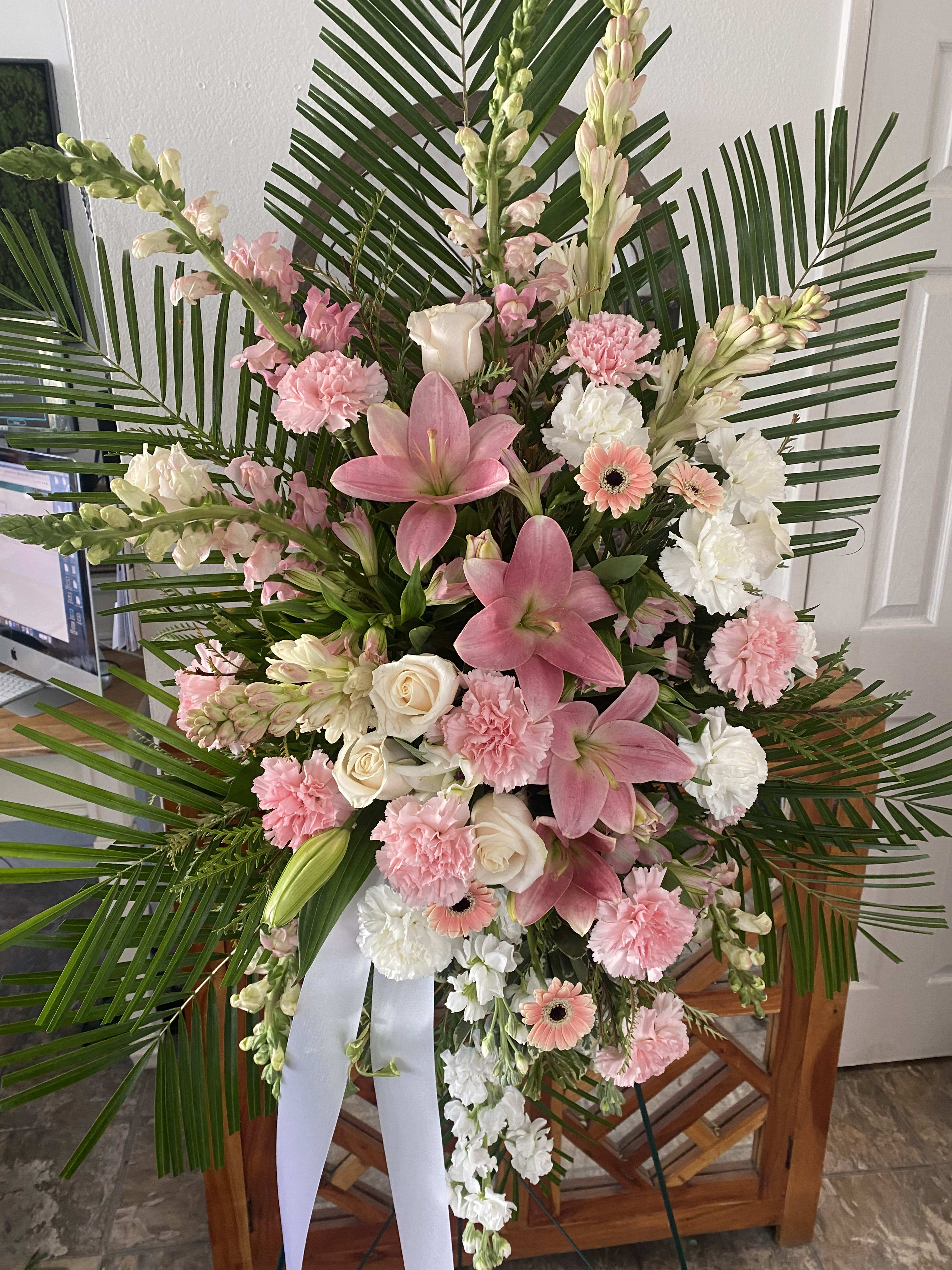 Pink and white floral standing spray with palm fronds and a white ribbon