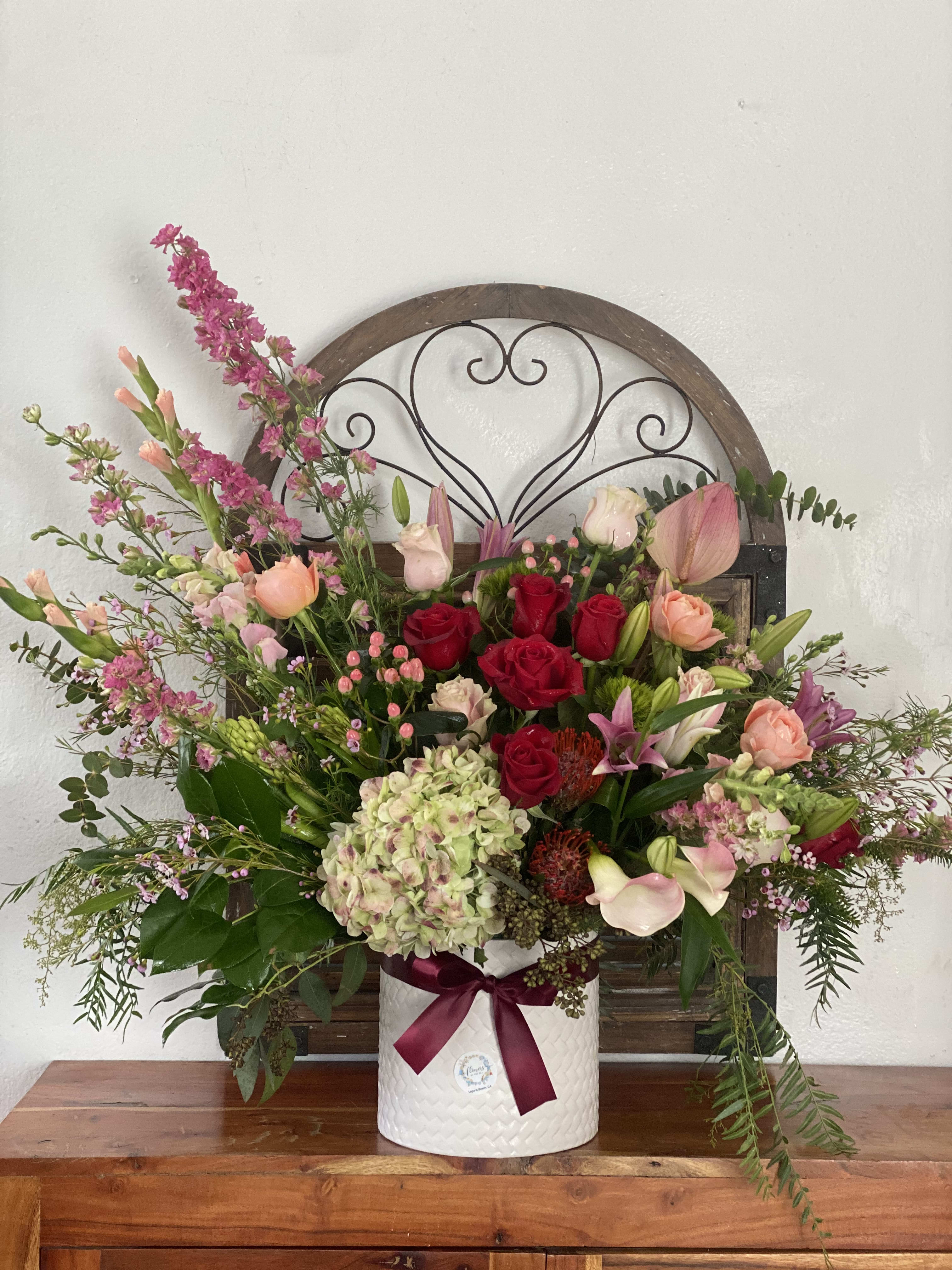 Mixed bouquet of roses, lilies, and hydrangea in a white vase with a ribbon
