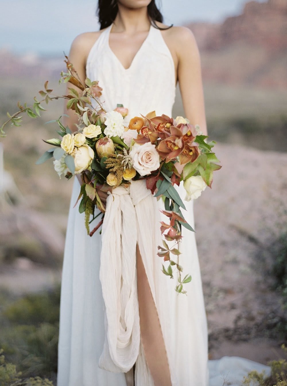Bride holding a cascading bouquet of cream, peach, and rust flowers