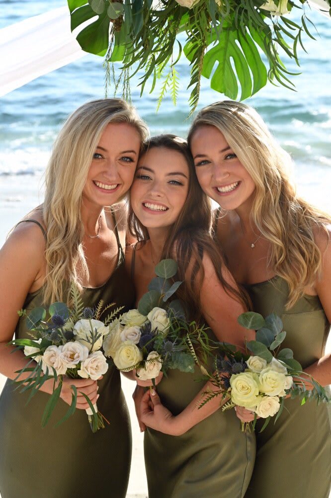 Three women holding small bouquets on a beach