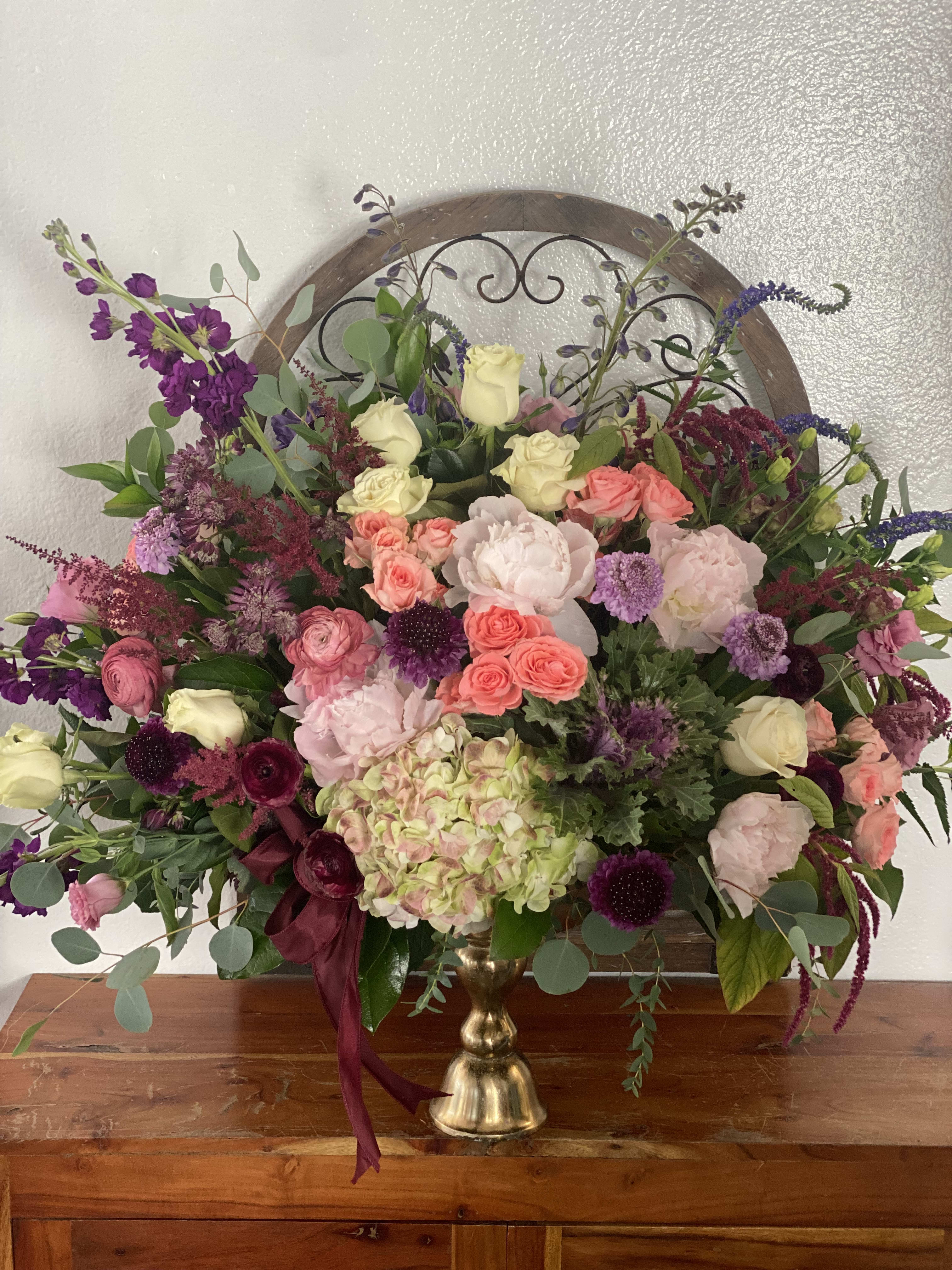 Large mixed floral arrangement in a gold vase with pink, purple, and cream blooms