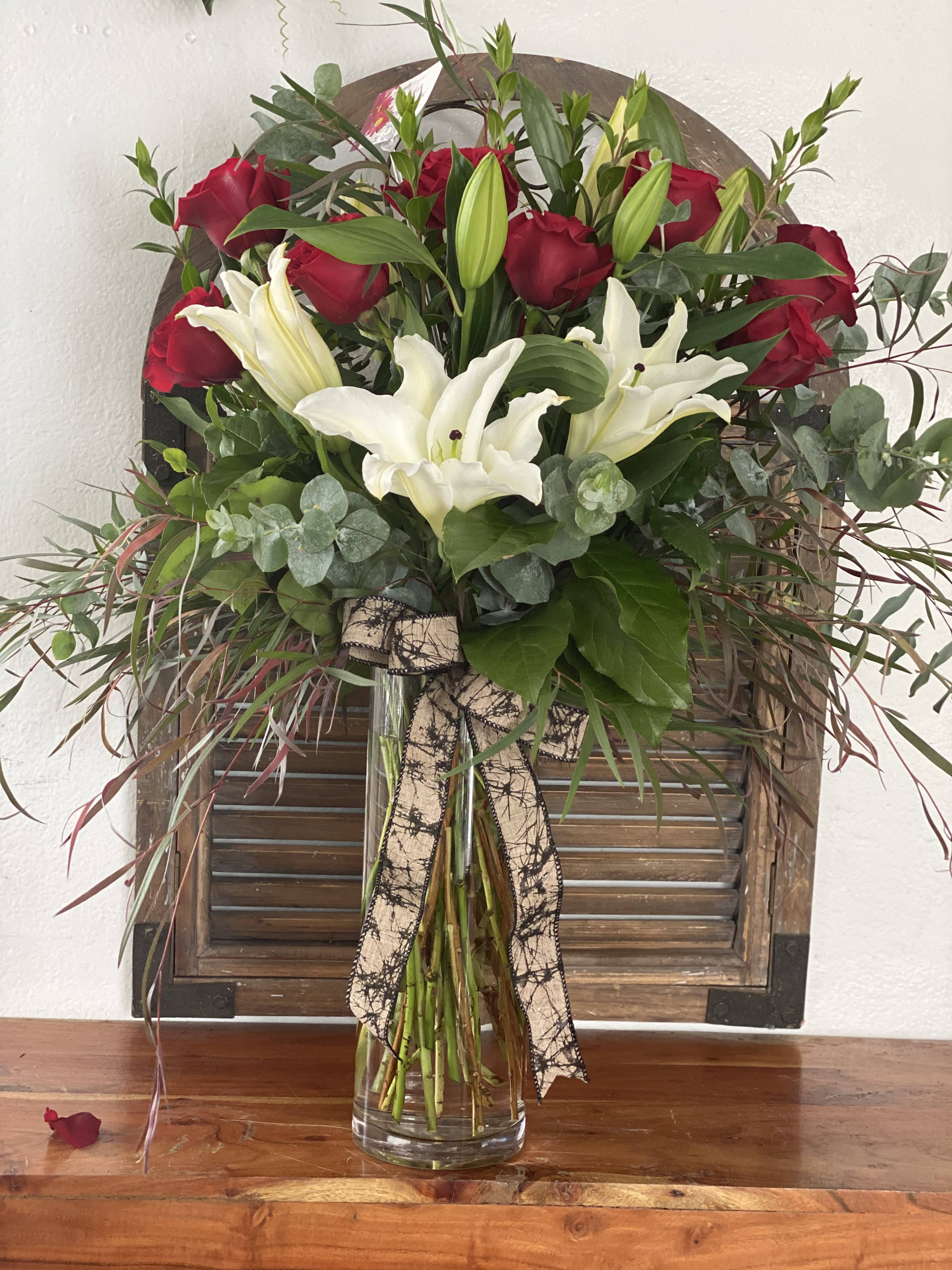 Red roses and white lilies in a clear glass vase with a ribbon