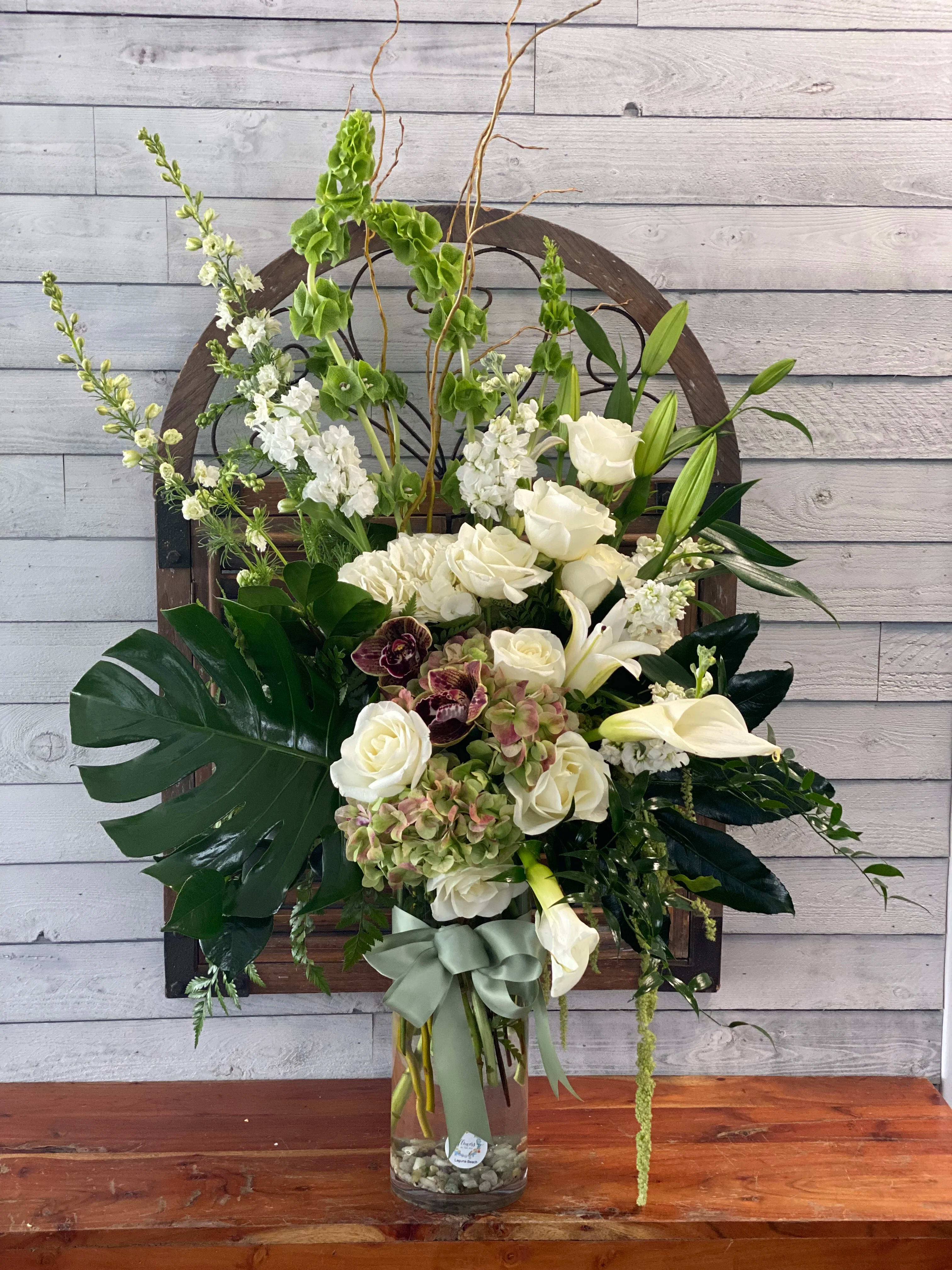 Tall white floral arrangement in a glass vase with a sage ribbon