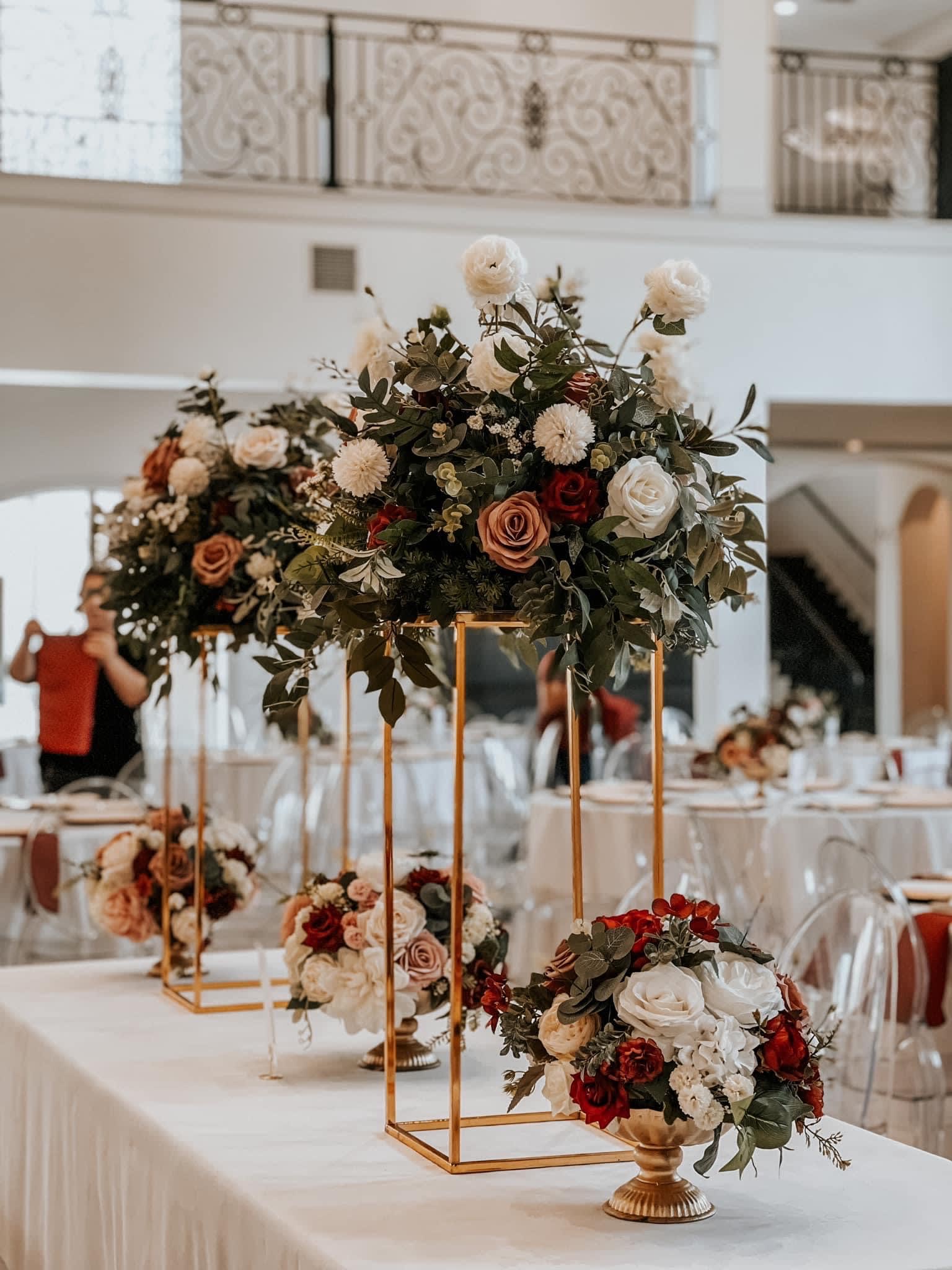 Tall floral centerpieces with roses and greenery on gold stands at a reception table