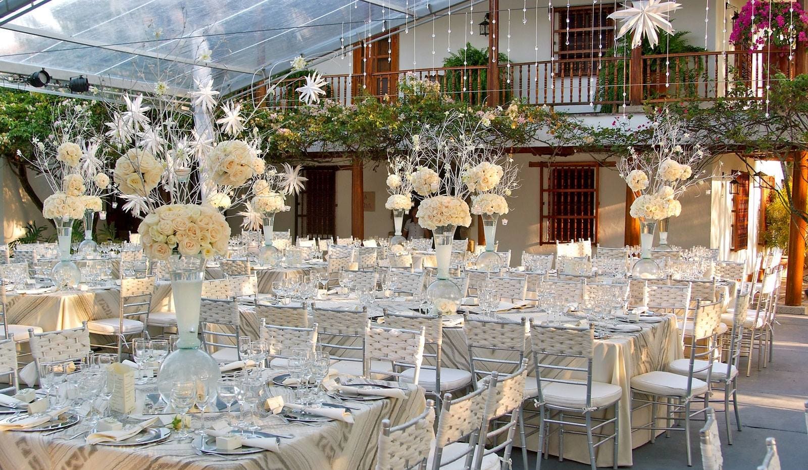 White floral centerpieces on long banquet tables at an outdoor event.