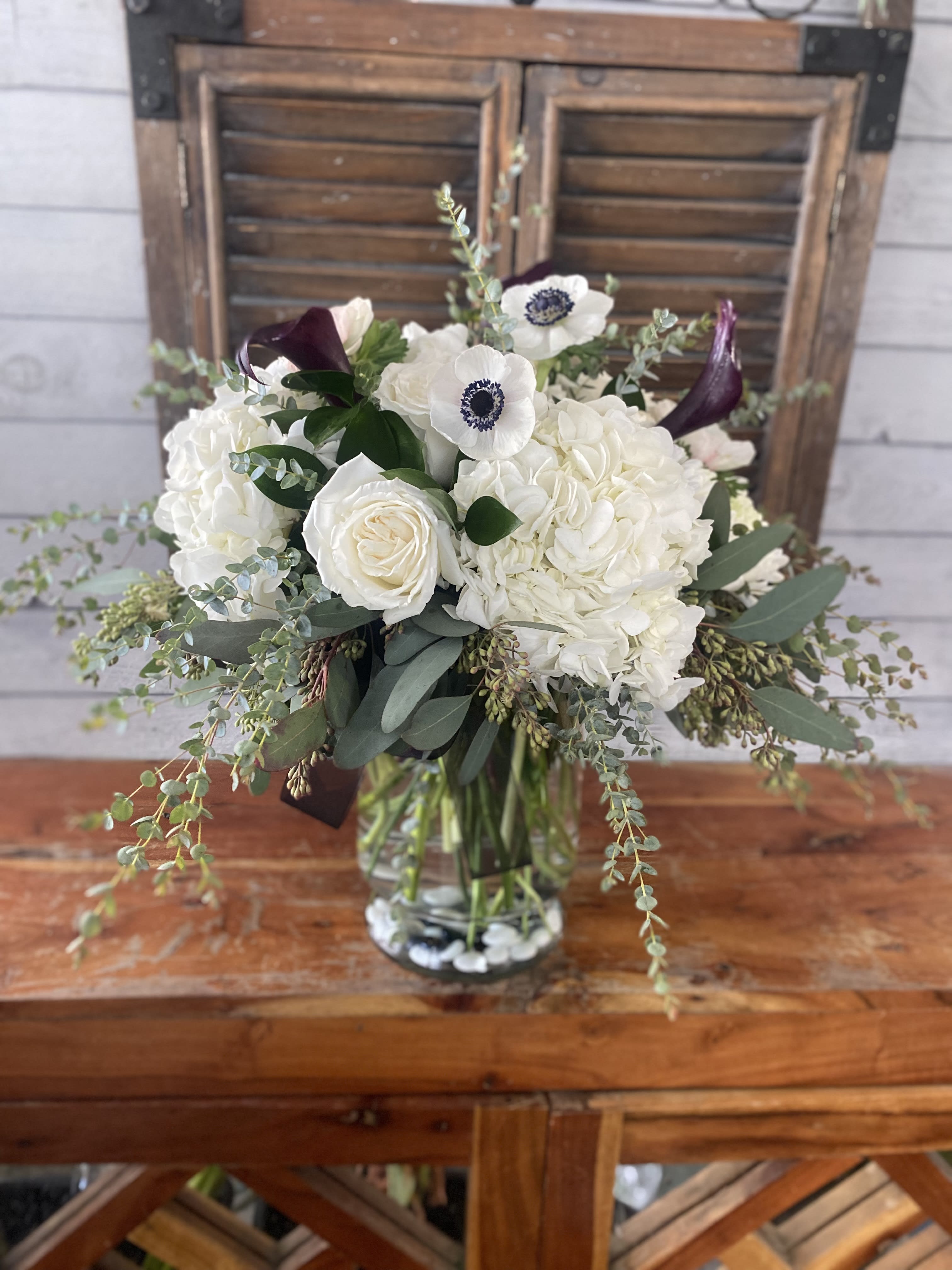 White bouquet with roses, hydrangeas, and dark calla lilies in a glass vase